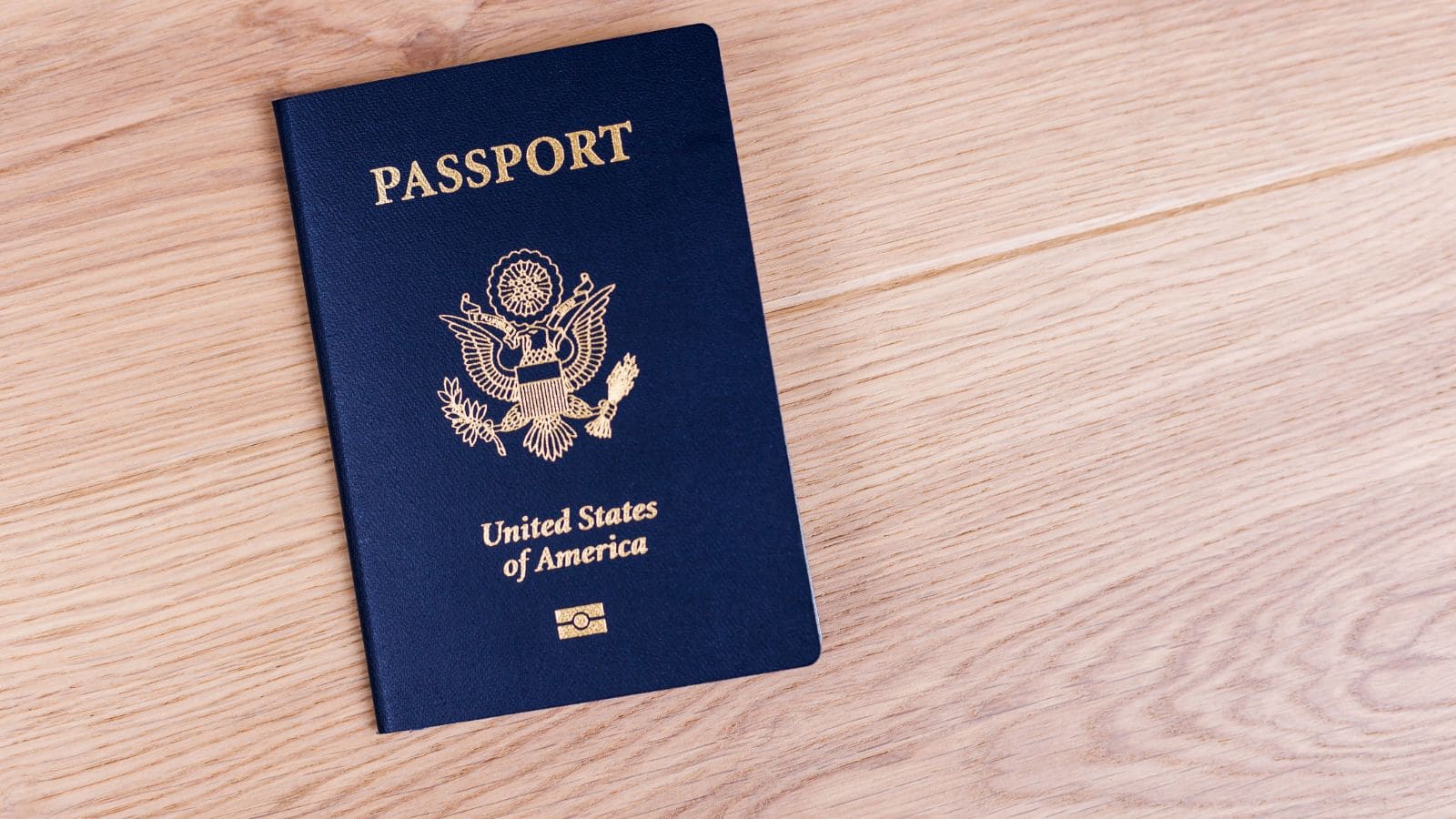 A United States passport with a navy blue cover lies on a light wooden surface.