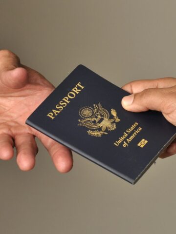Two people exchanging a United States passport, one hand receiving and one hand giving.