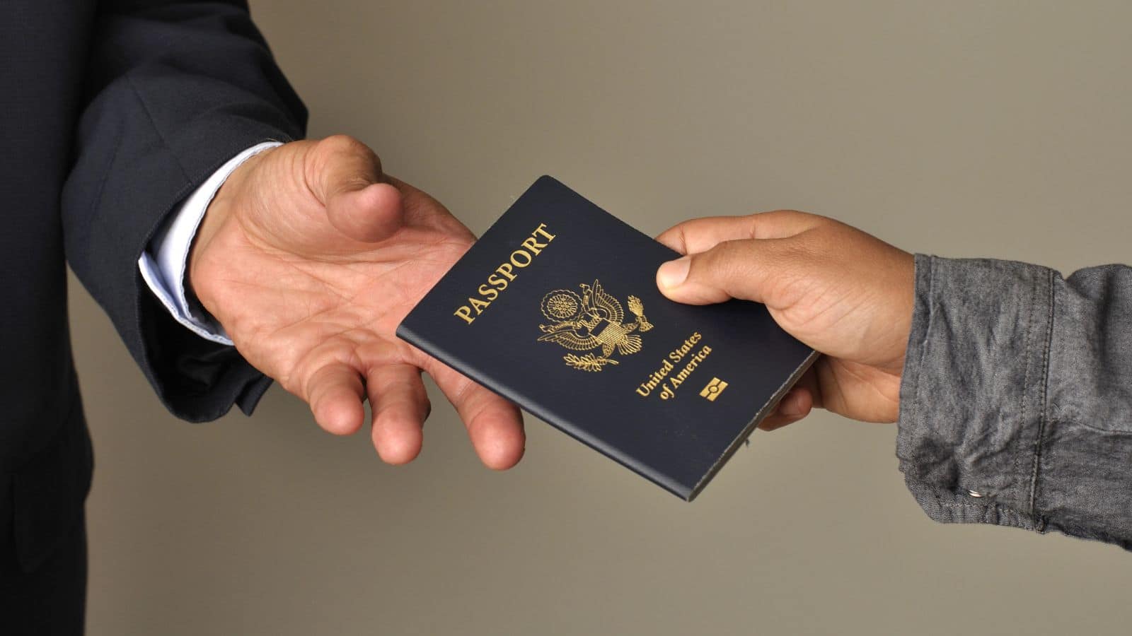 Two people exchanging a United States passport, one hand receiving and one hand giving.