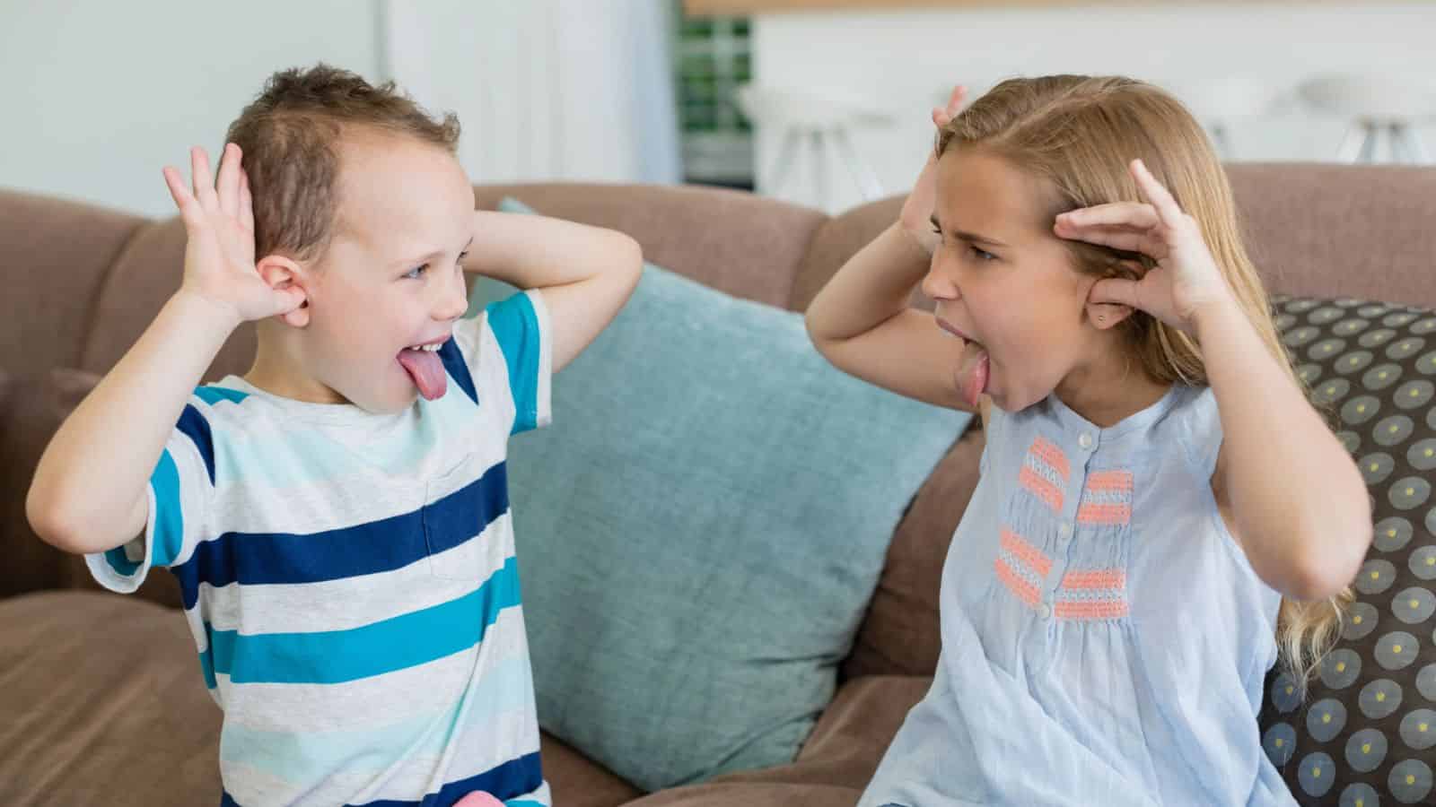 Two children on a couch making funny faces and sticking out their tongues at each other.