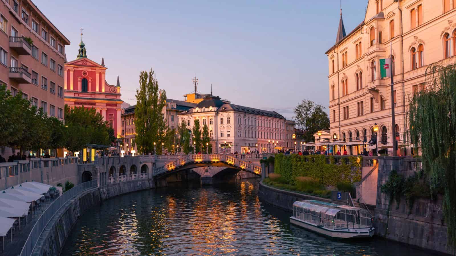 A serene river with a bridge, historic buildings, and a boat at sunset in a European city.