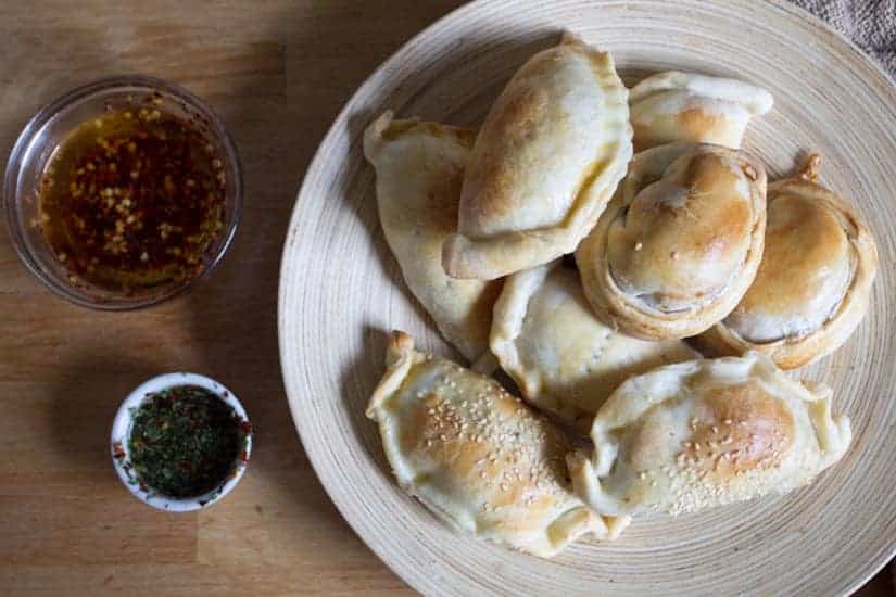 A plate of baked empanadas, a classic Colombian street food, with two small bowls of dipping sauces on a wooden table.