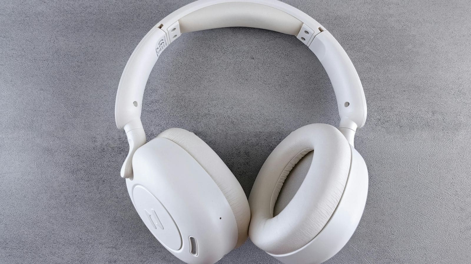 White over-ear wireless headphones on a gray textured surface, displayed from above.