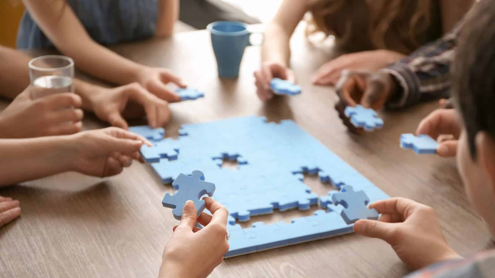 Several people work together to assemble a blue jigsaw puzzle on a wooden table.