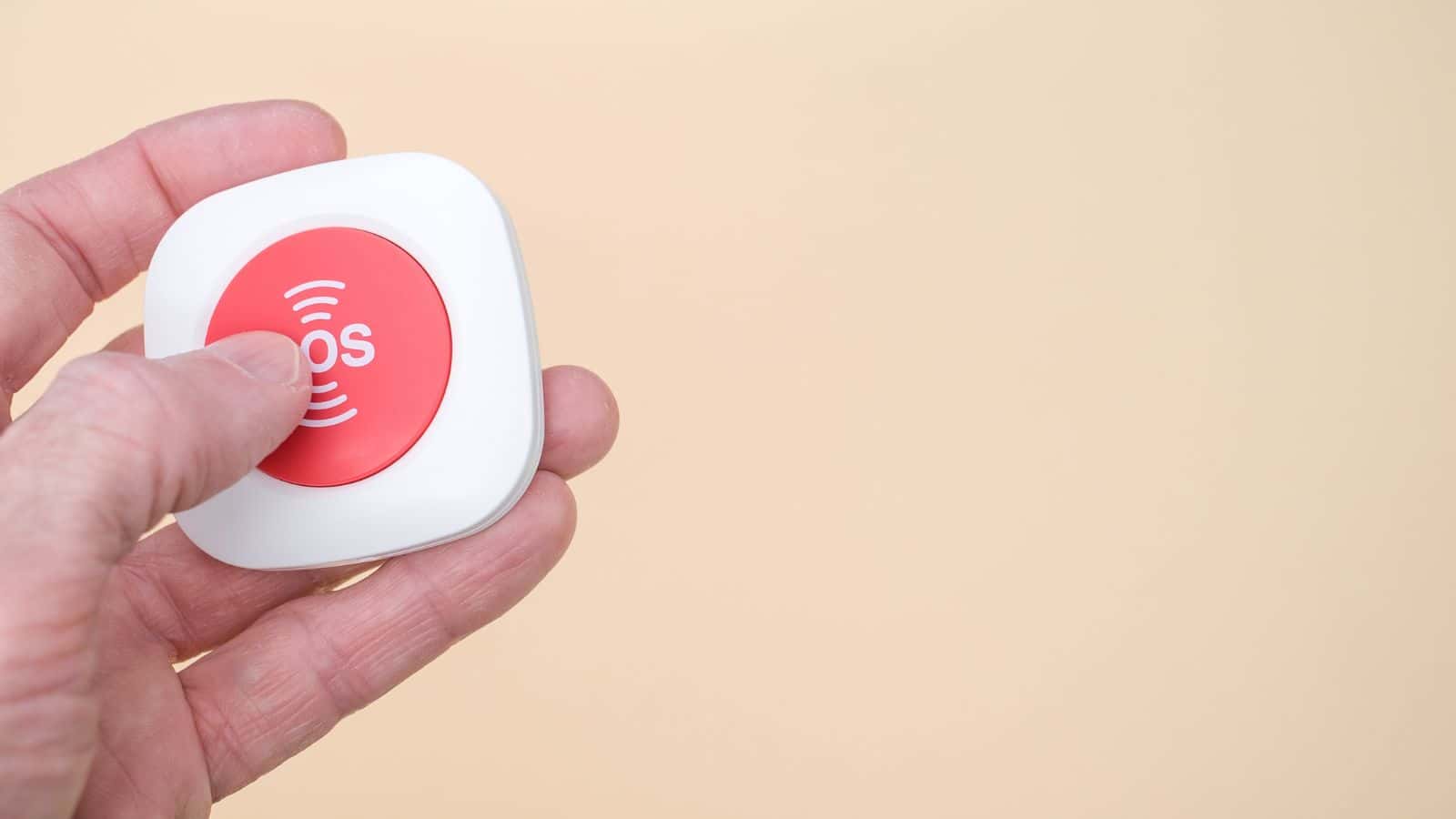 A hand pressing a red SOS button on a small white device against a beige background.
