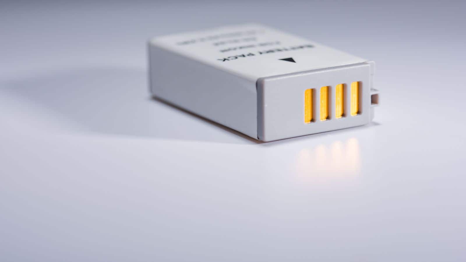 A close-up of a white battery pack with yellow contacts on a plain white surface.