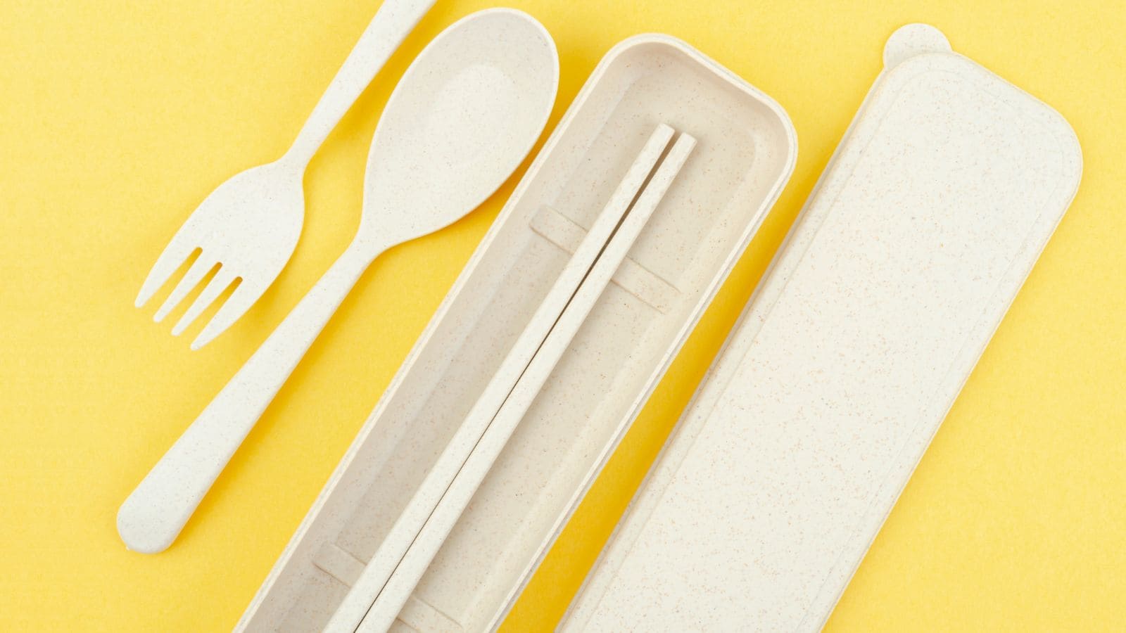 Beige spoon, fork, and chopsticks with a matching case on a yellow background.