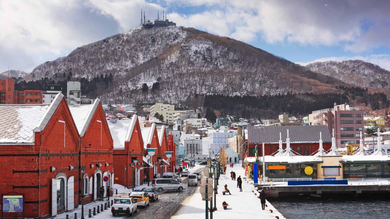 Red brick warehouses and snowy streets with a mountain in the background, under a partly cloudy sky.