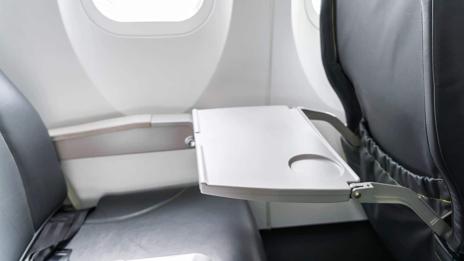 An airplane tray table is open and attached to the back of the seat in front of a window seat, offering convenience for plane travel and making it easier to enjoy meals or organize your travel products during your flight.