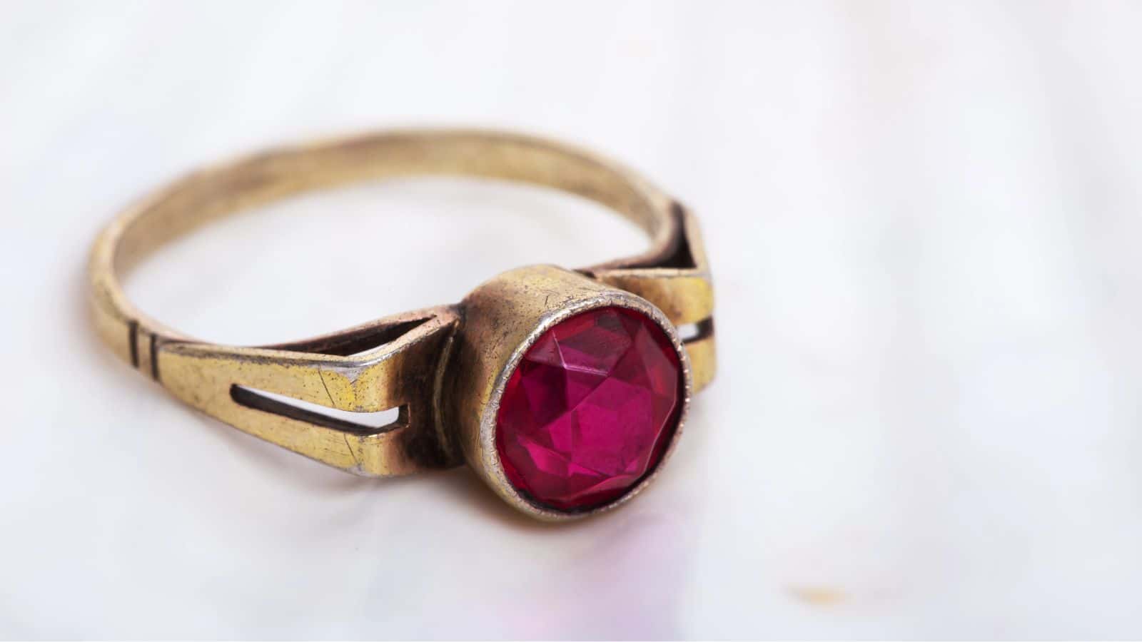 A gold ring with a large round red gemstone set in the center, displayed on a light background.