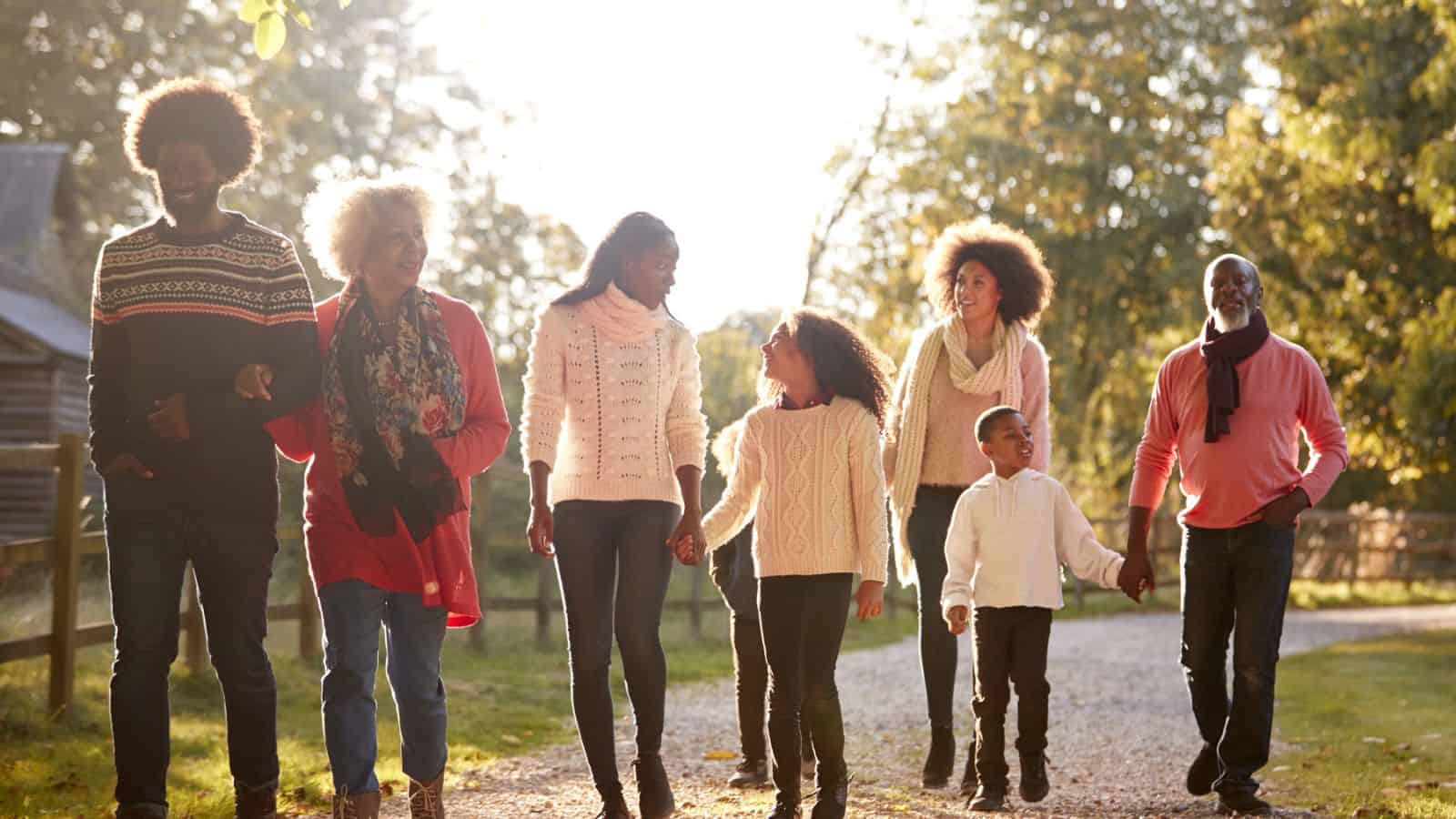 Three generations of a family walk together outdoors on a sunny day, smiling and talking.