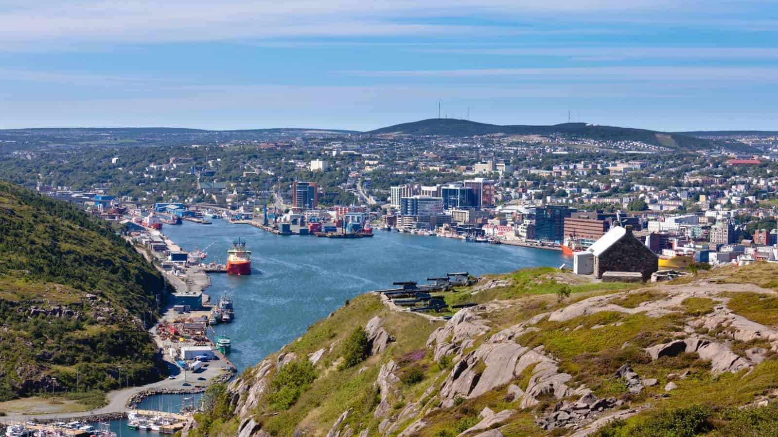 A scenic view of a harbor city with hills, boats, and buildings under a blue sky.