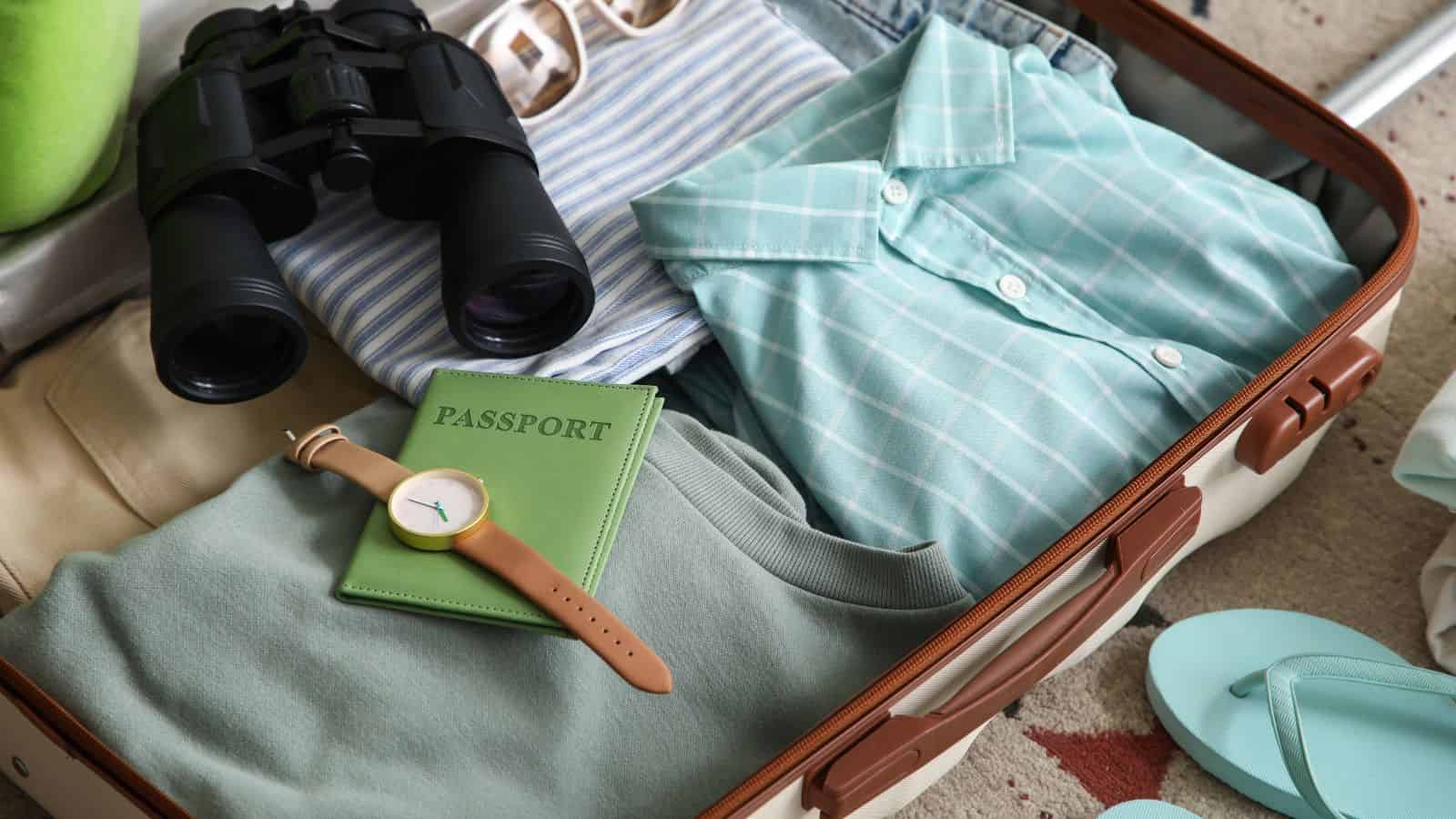 Open suitcase with clothes, binoculars, a passport, a wristwatch, and flip-flops neatly packed inside.