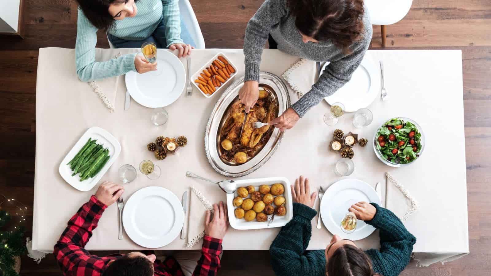 Four people sit around a table with roast chicken, potatoes, green beans, carrots, and salad.