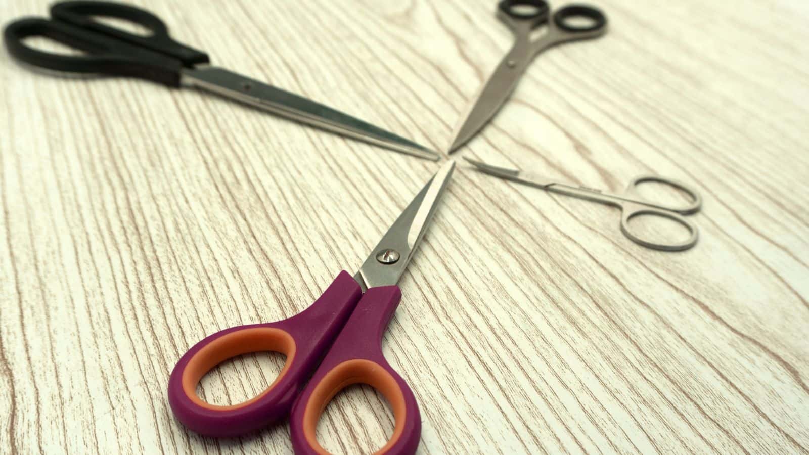 Three pairs of scissors with different handles arranged on a light wood surface, forming a triangle shape.