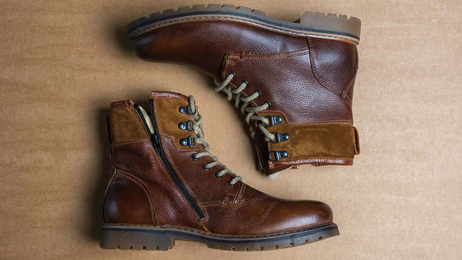 A pair of brown leather lace-up boots with side zippers, displayed on a tan surface.