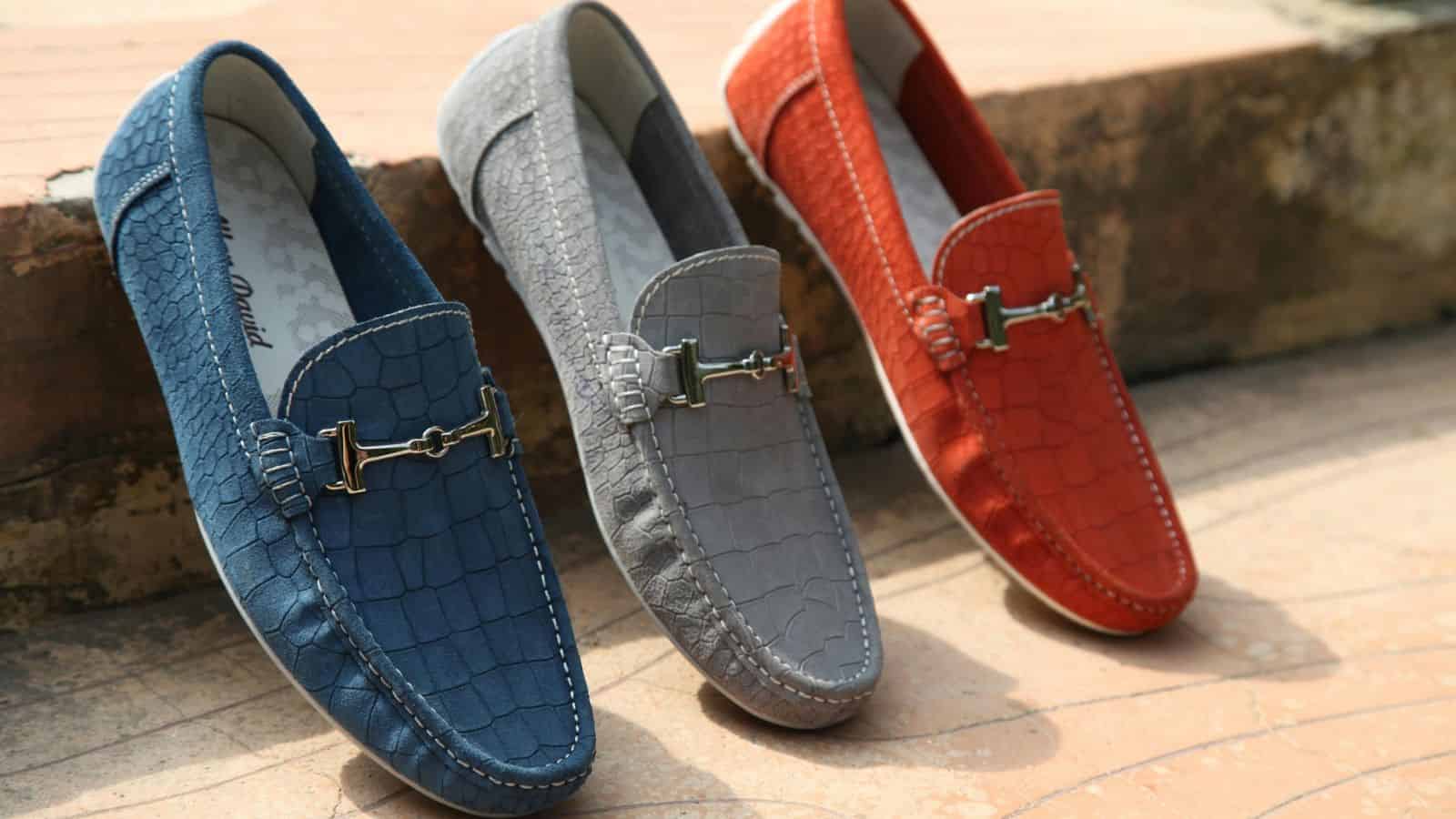 Three textured loafers in blue, gray, and red are displayed on a stone surface in sunlight—perfect for making holiday airports less stressful with comfortable, stylish footwear.