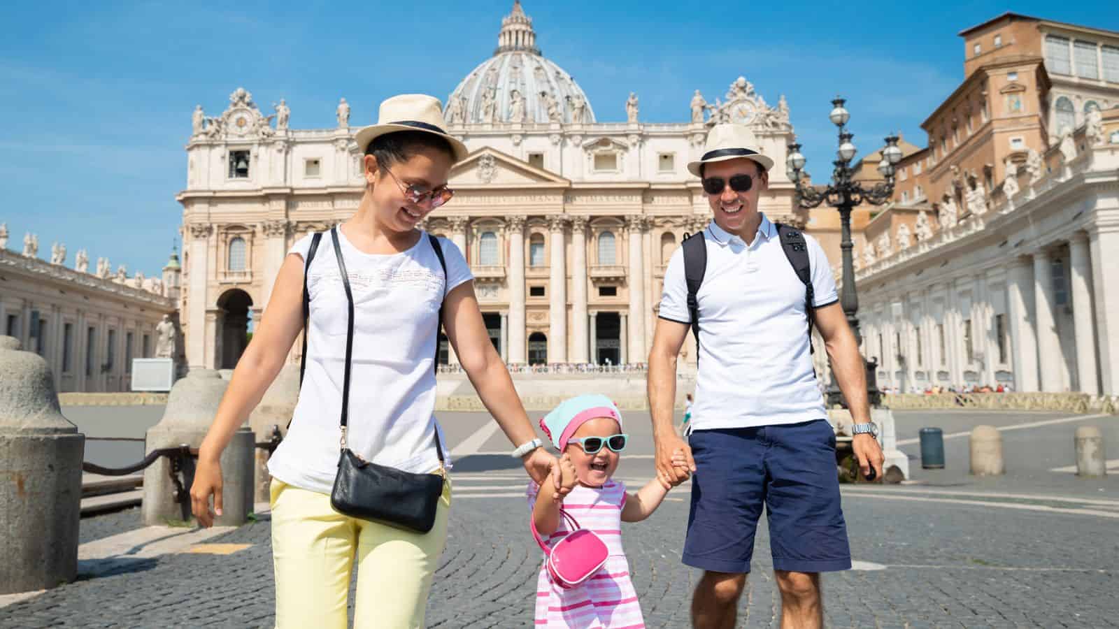 Smiling family with a toddler walking in front of a grand historic building on a sunny day.