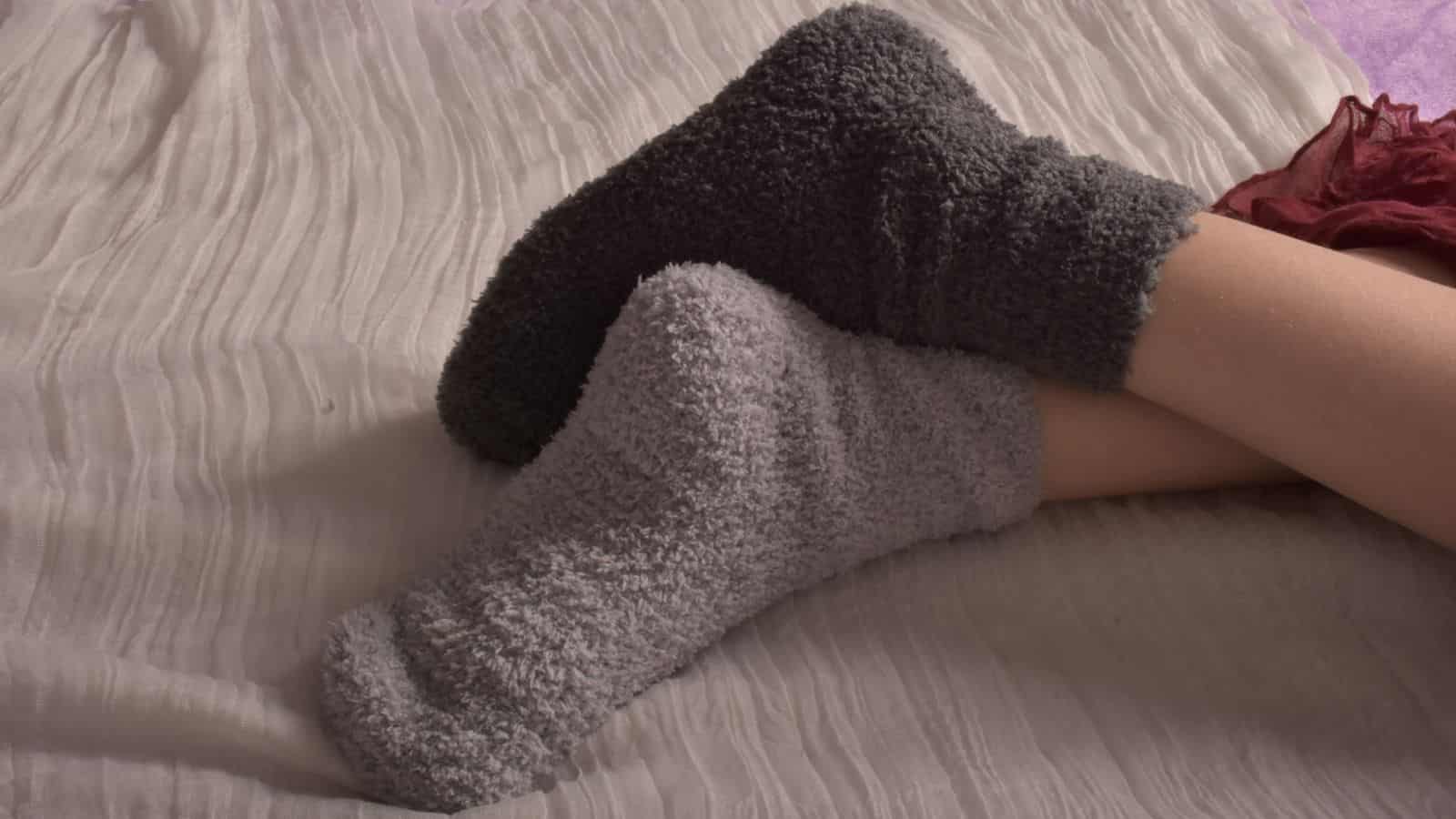 Two crossed legs wearing cozy, fuzzy socks on a soft, light-colored fabric surface.