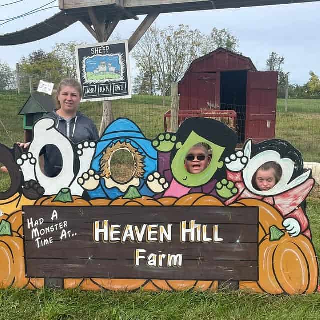 Three people pose with their faces in cutouts at Heaven Hill Farm, standing behind a monster-themed sign—one of the best pumpkin patches for festive family fun.