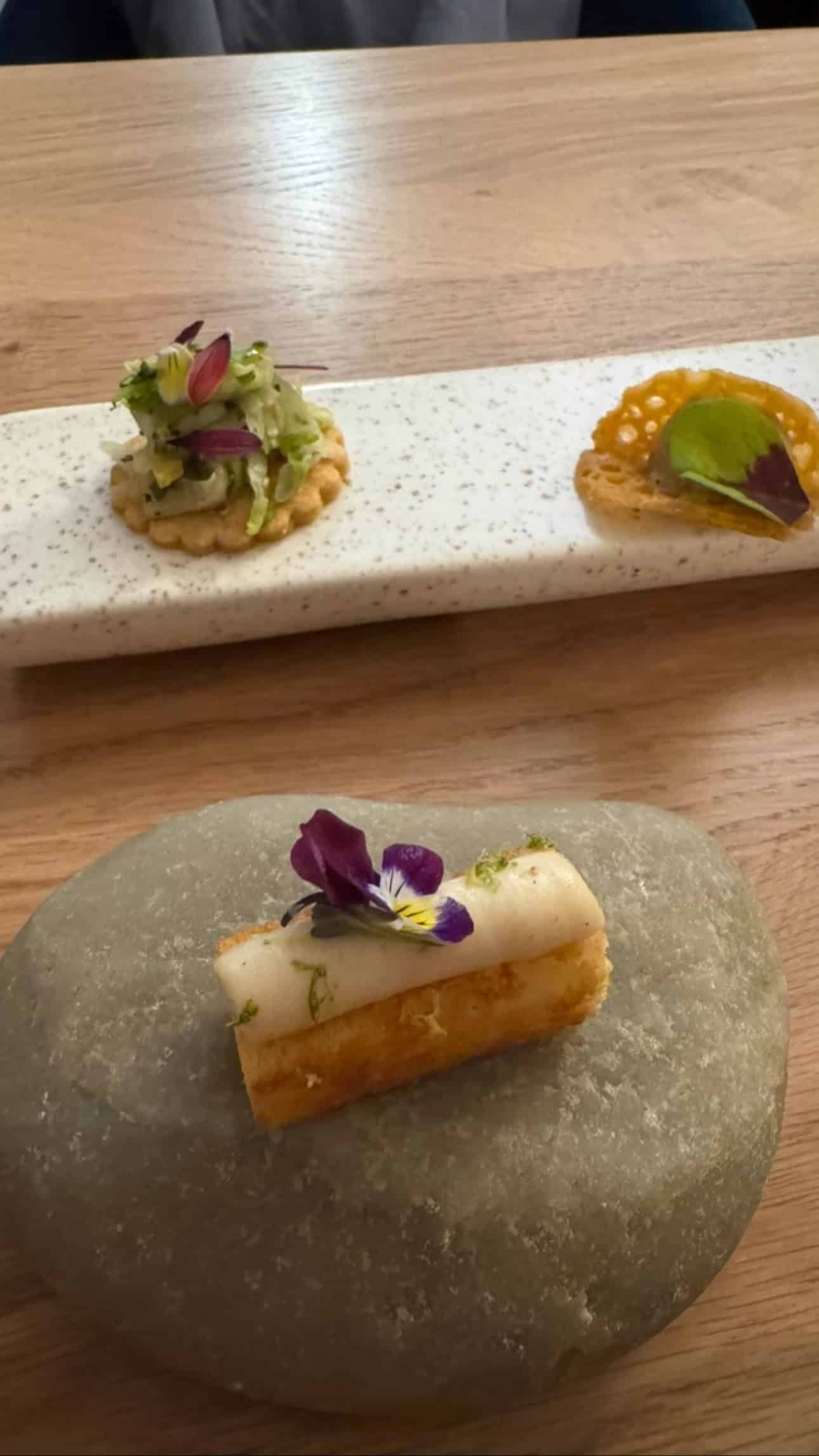 Three elegant appetizers, each garnished with herbs and edible flowers, evoke the flavors of Marseille and are beautifully served on stone and ceramic plates.