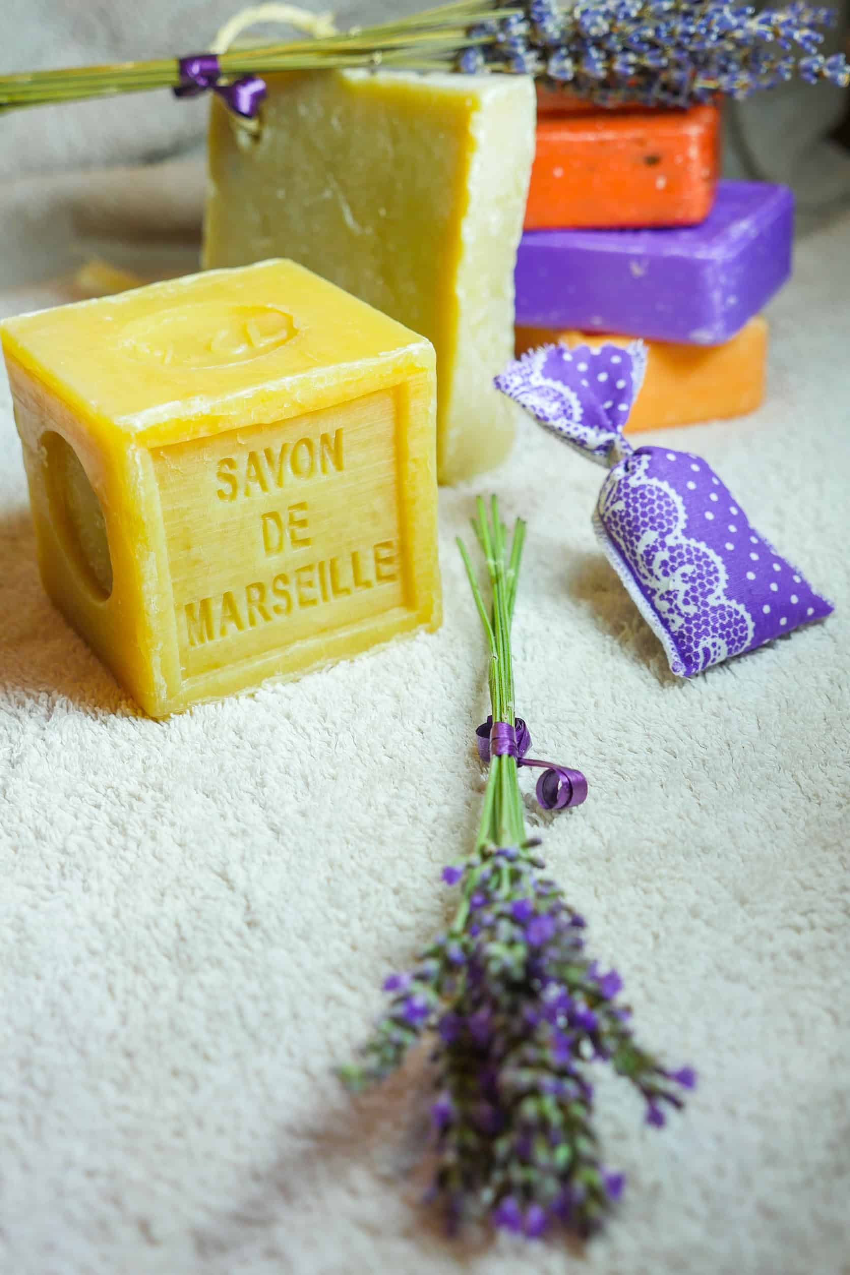 Yellow Savon de Marseille soap, lavender sprigs, a sachet, and colorful soaps create a charming scene reminiscent of a France itinerary on a soft surface.