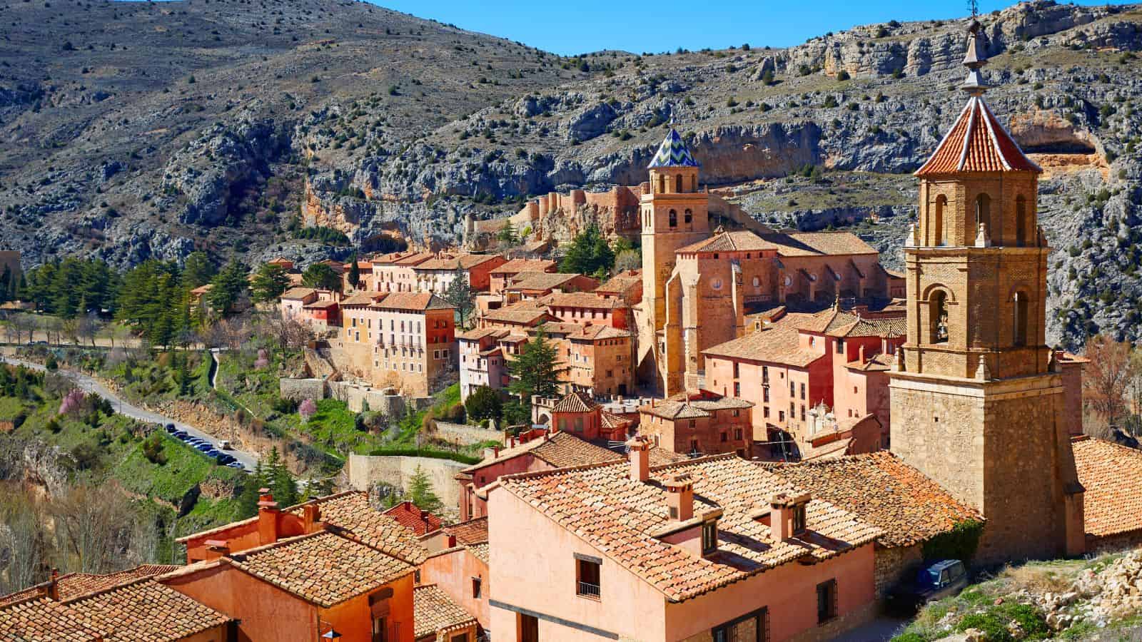 A hilltop village with terracotta rooftops and a church tower, set against rocky, mountainous terrain.