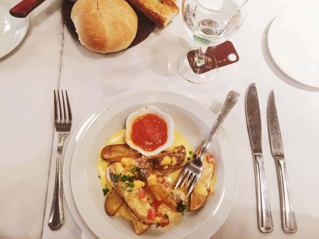 Plate of potato wedges with sauce, a bread roll, and cutlery on a white tablecloth—perfect comfort food after exploring things to do in Buenos Aires.