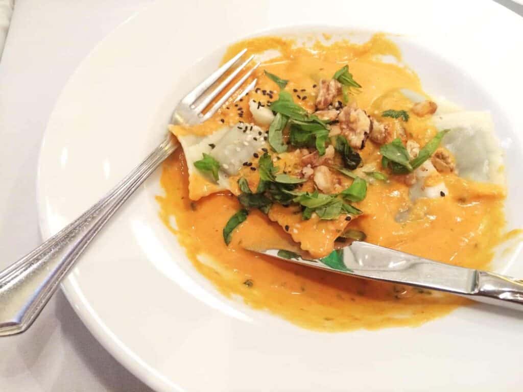 Ravioli with orange sauce, topped with herbs and nuts, served on a white plate with a fork and knife—a delightful dish that’s among the must-try things to do in Buenos Aires for food lovers.