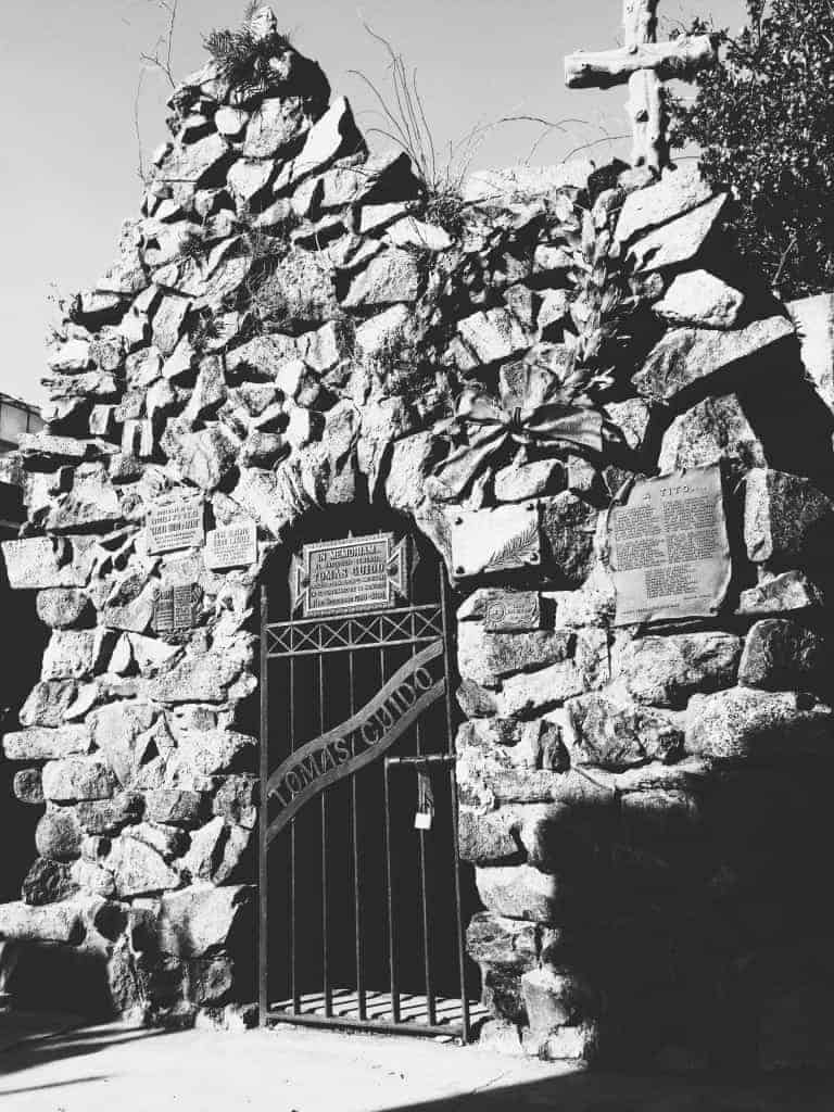 Black and white photo of a stone mausoleum with plaques, a gated door, and a cross on top—a haunting reminder of the unique things to do in Buenos Aires.