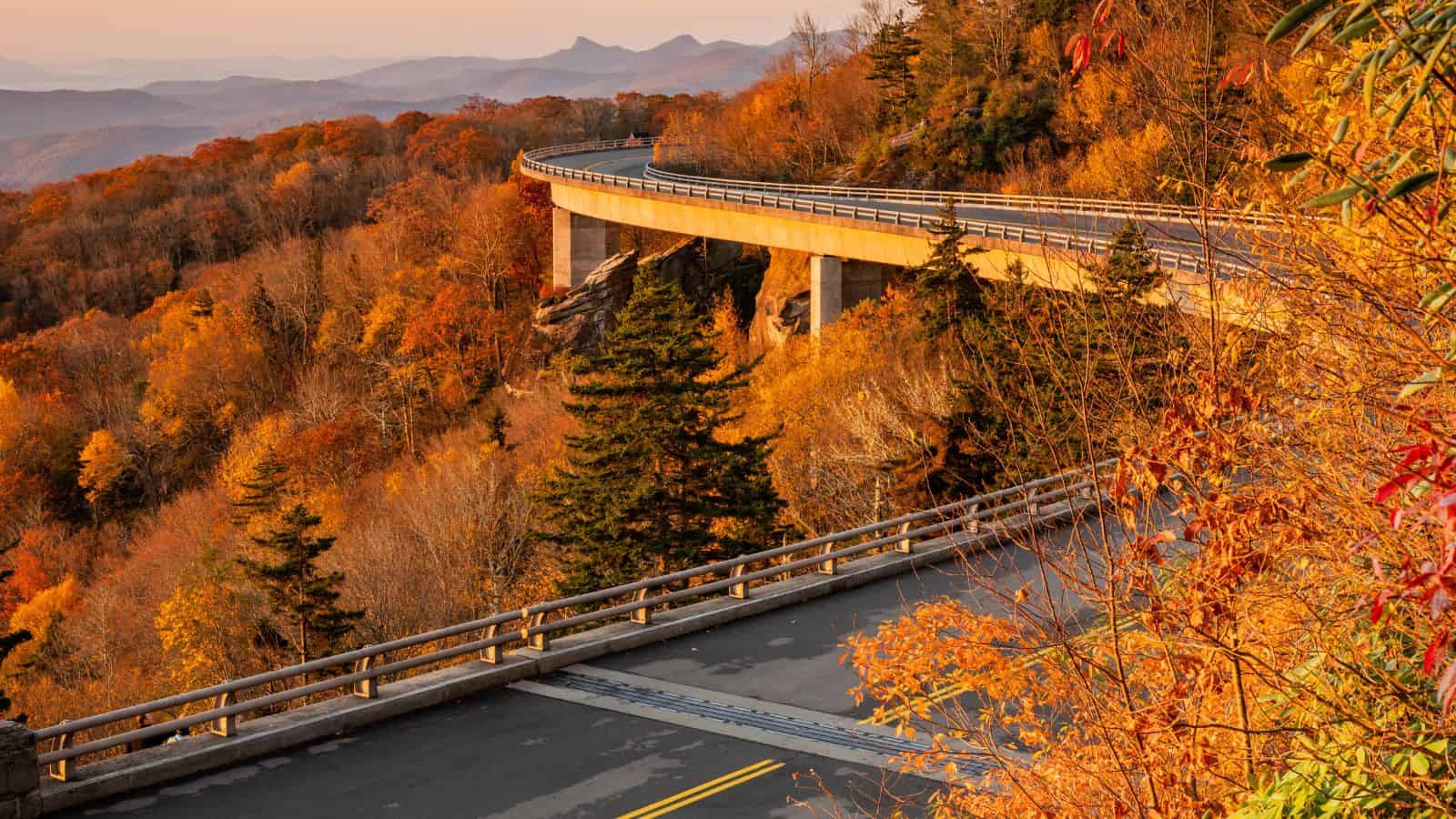 Curving bridge through colorful autumn trees on a mountain, with distant peaks under a clear sky&mdash;a perfect scene for fall destinations and memorable weekend getaways.