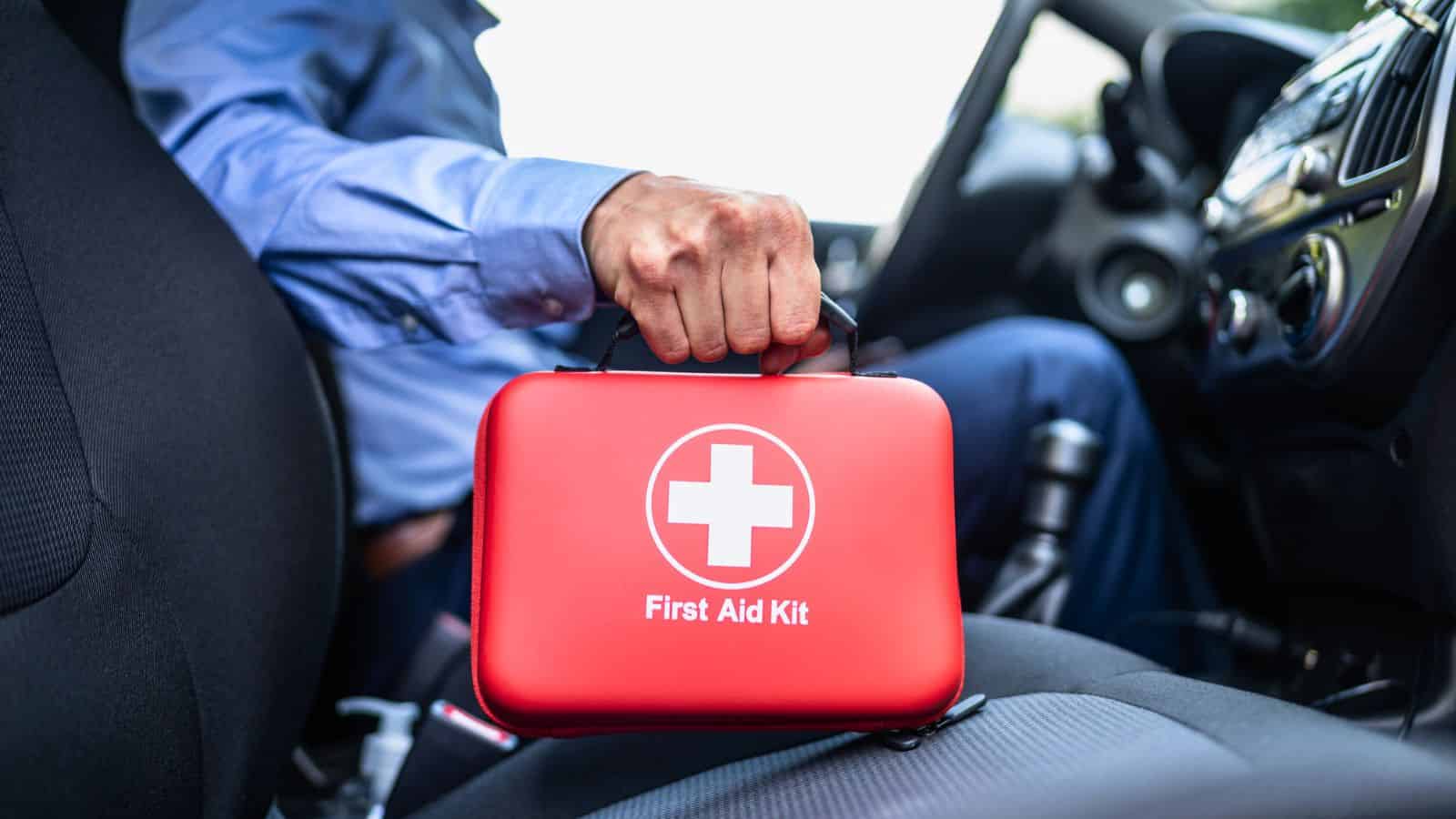 Person holding a red first aid kit inside a car, placing it on the front passenger seat.