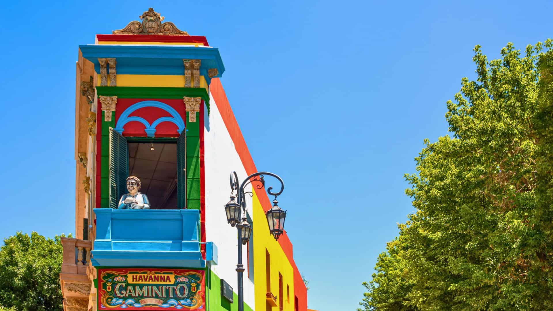 Colorful building with a balcony, statue, and street lamp in La Boca, Buenos Aires, under a clear blue sky.
