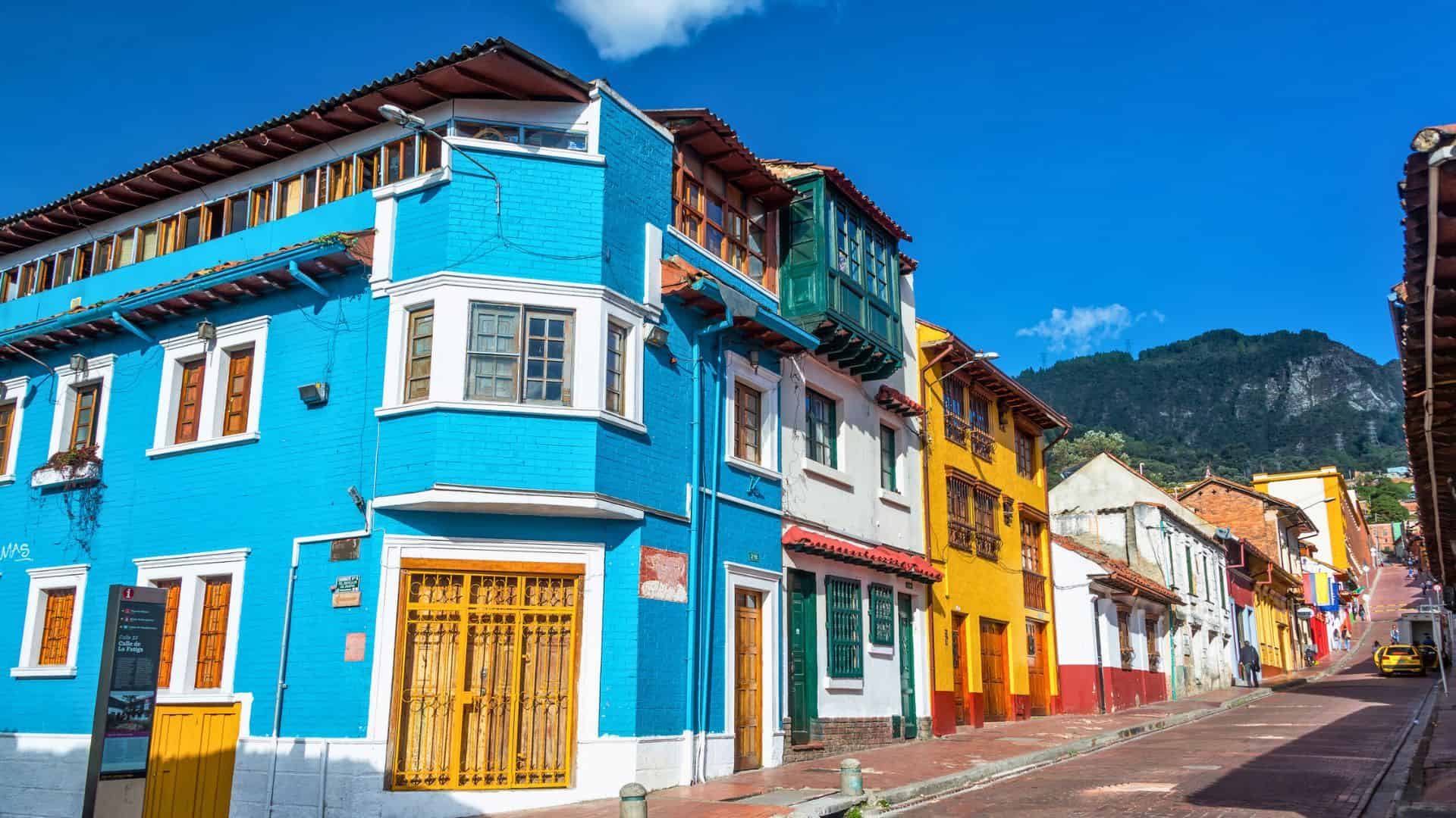 Colorful colonial buildings line a steep, sunny street with mountains in the background.