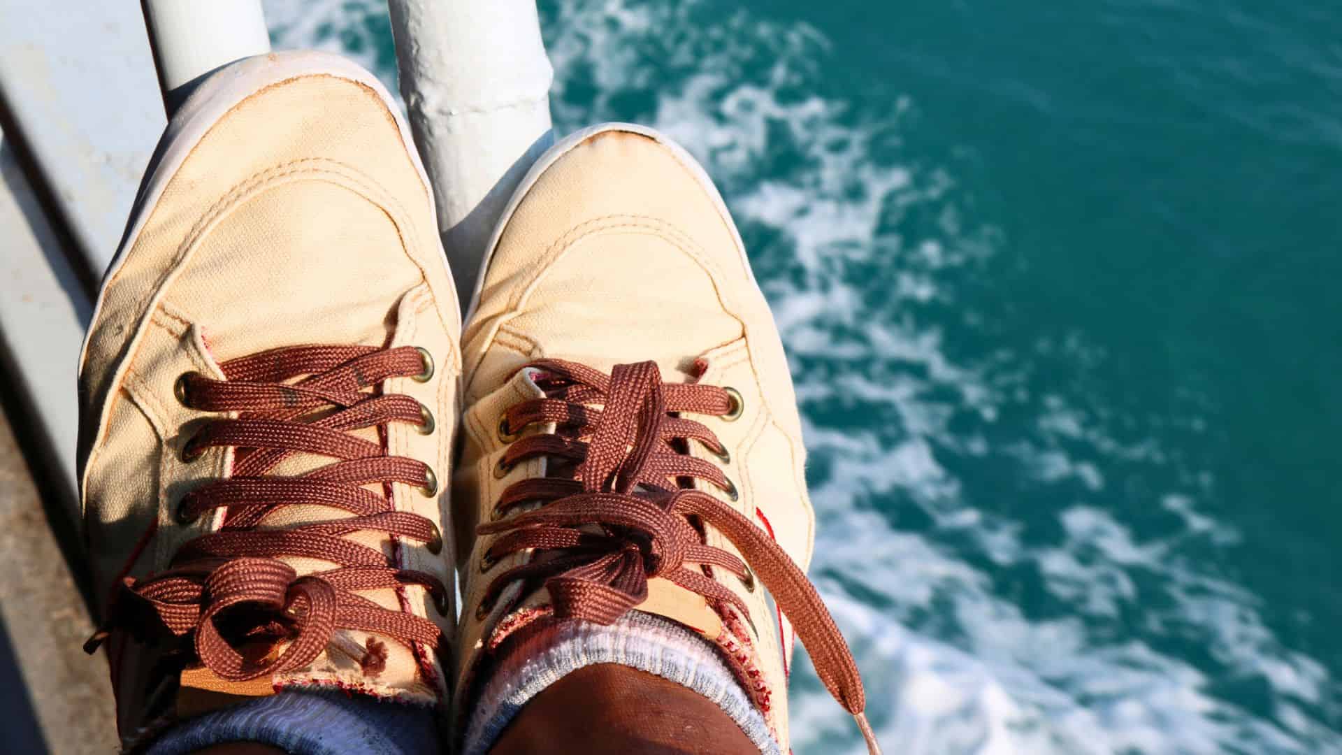 Two tan sneakers with brown laces resting by a railing above turquoise water.