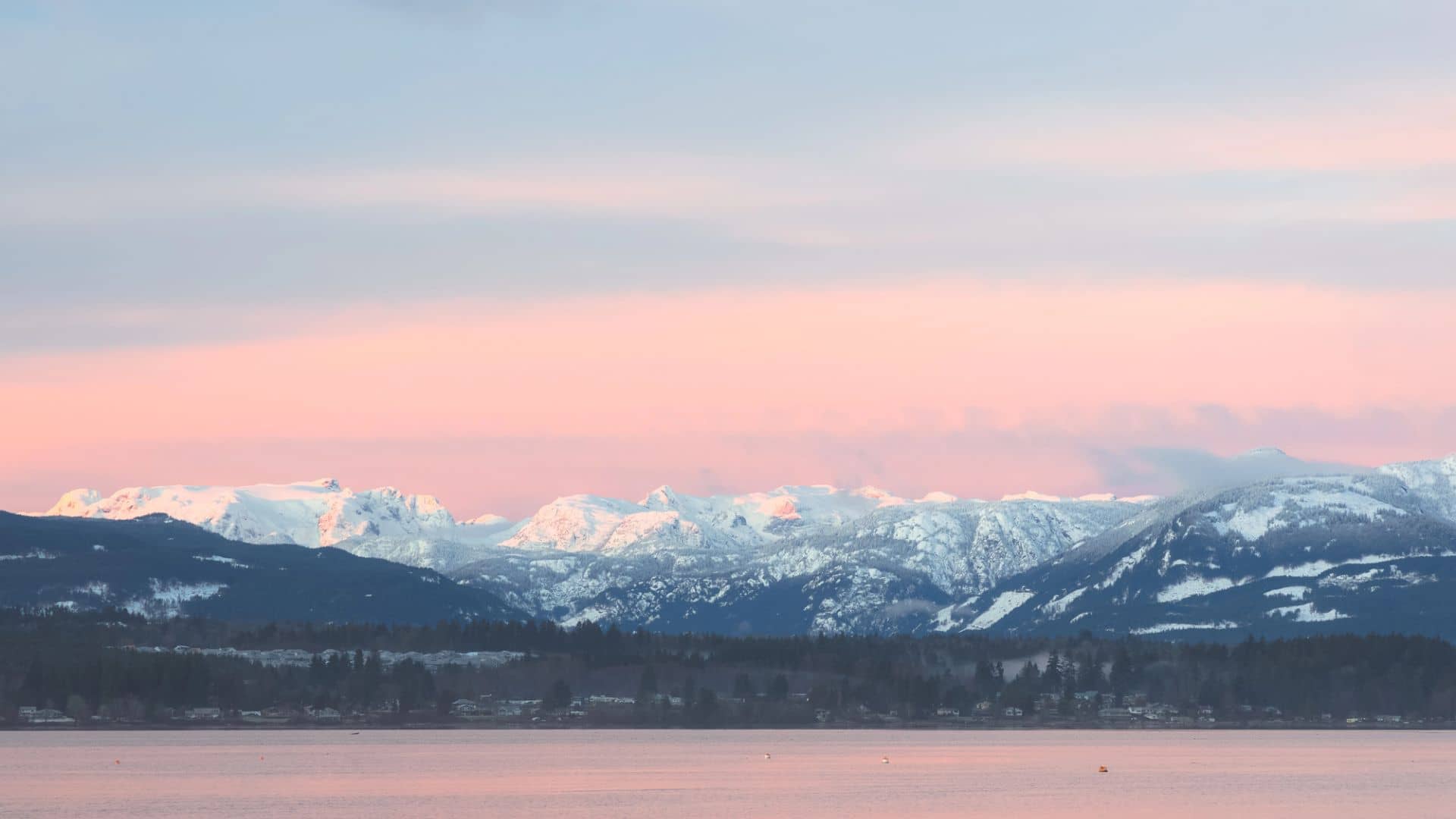 Snow-capped mountains under a pink and blue sky, reflected in a calm lake at sunset.