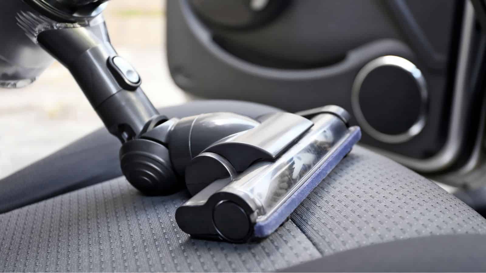 A vacuum cleaner head cleaning the fabric seat of a car interior.