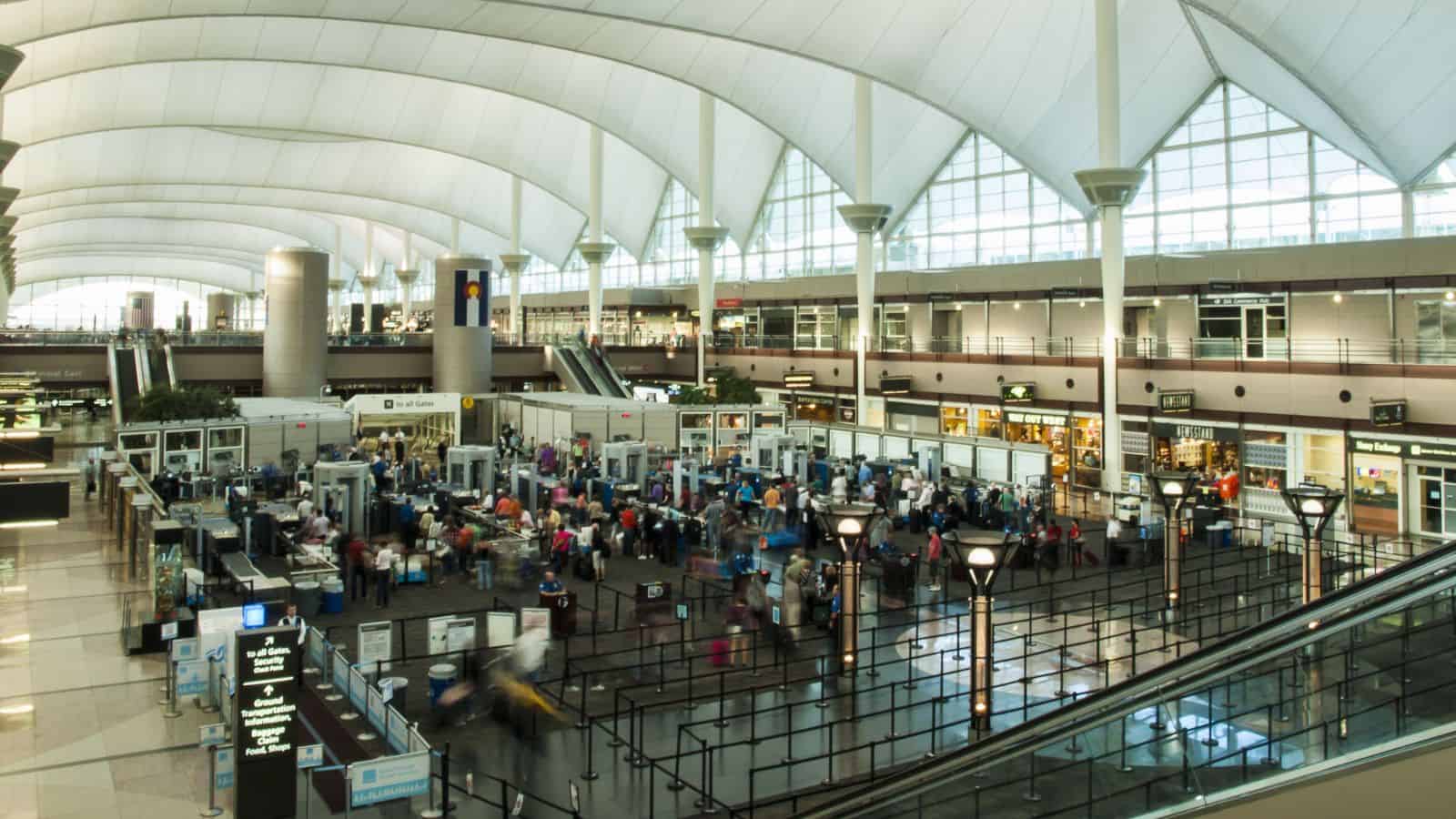 Wide view of a busy airport security checkpoint beneath a high, white curved ceiling.