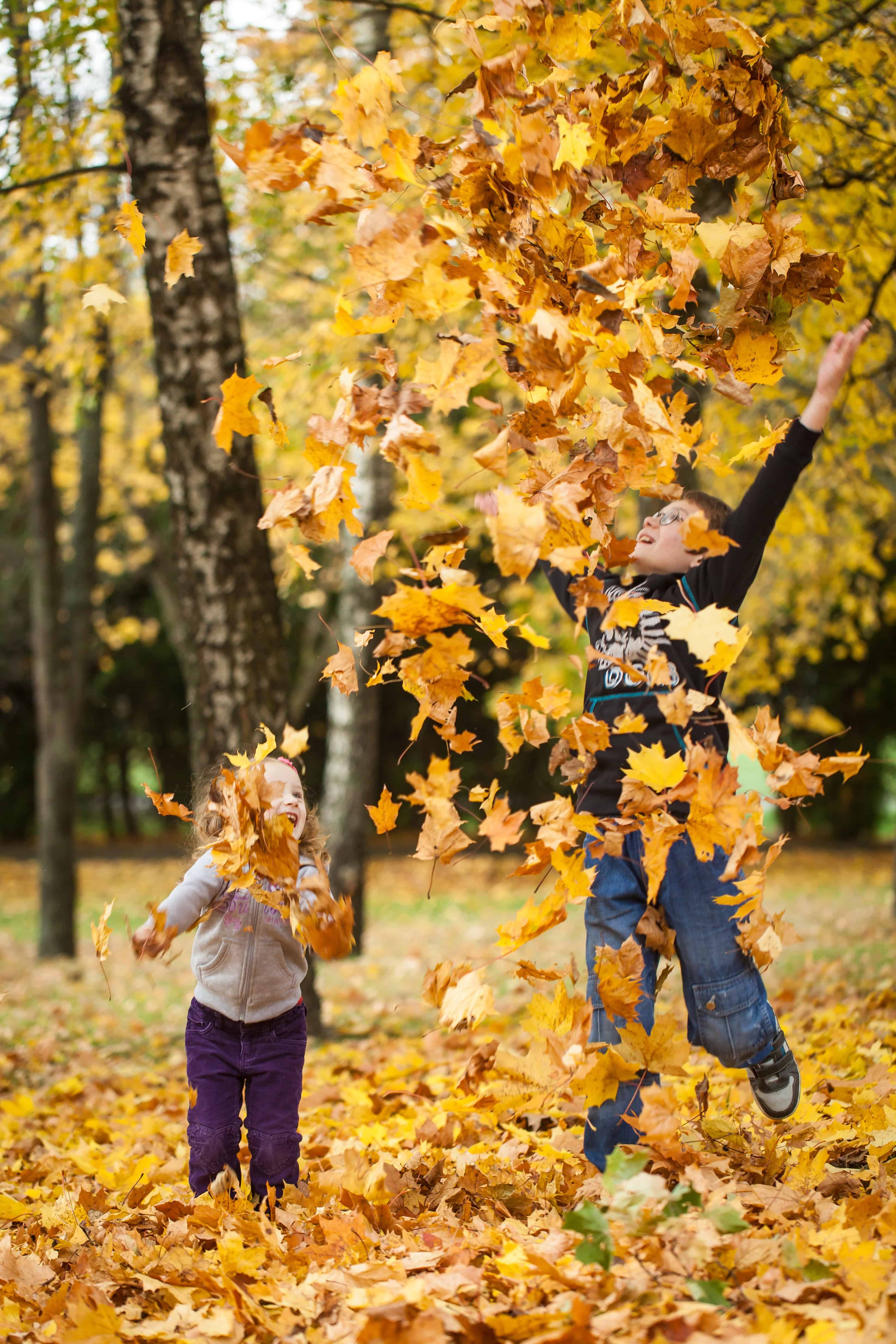 A boy and girl throwing leaves up in the air, enjoying some of the best fall foliage in USA.