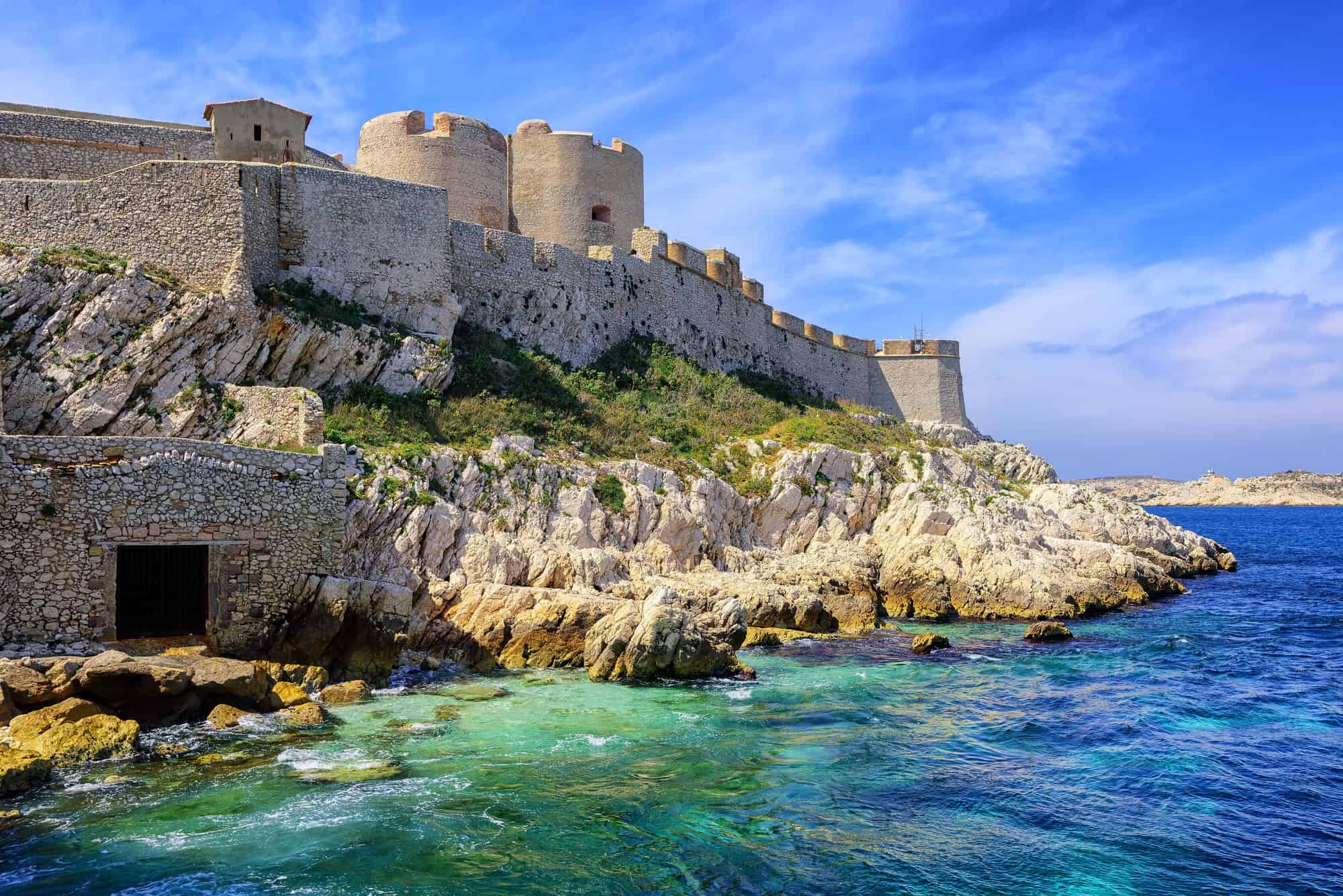 Ancient stone fortress on rocky coast near Marseille, France, overlooking the clear blue sea under a partly cloudy sky—a must-see on any itinerary.