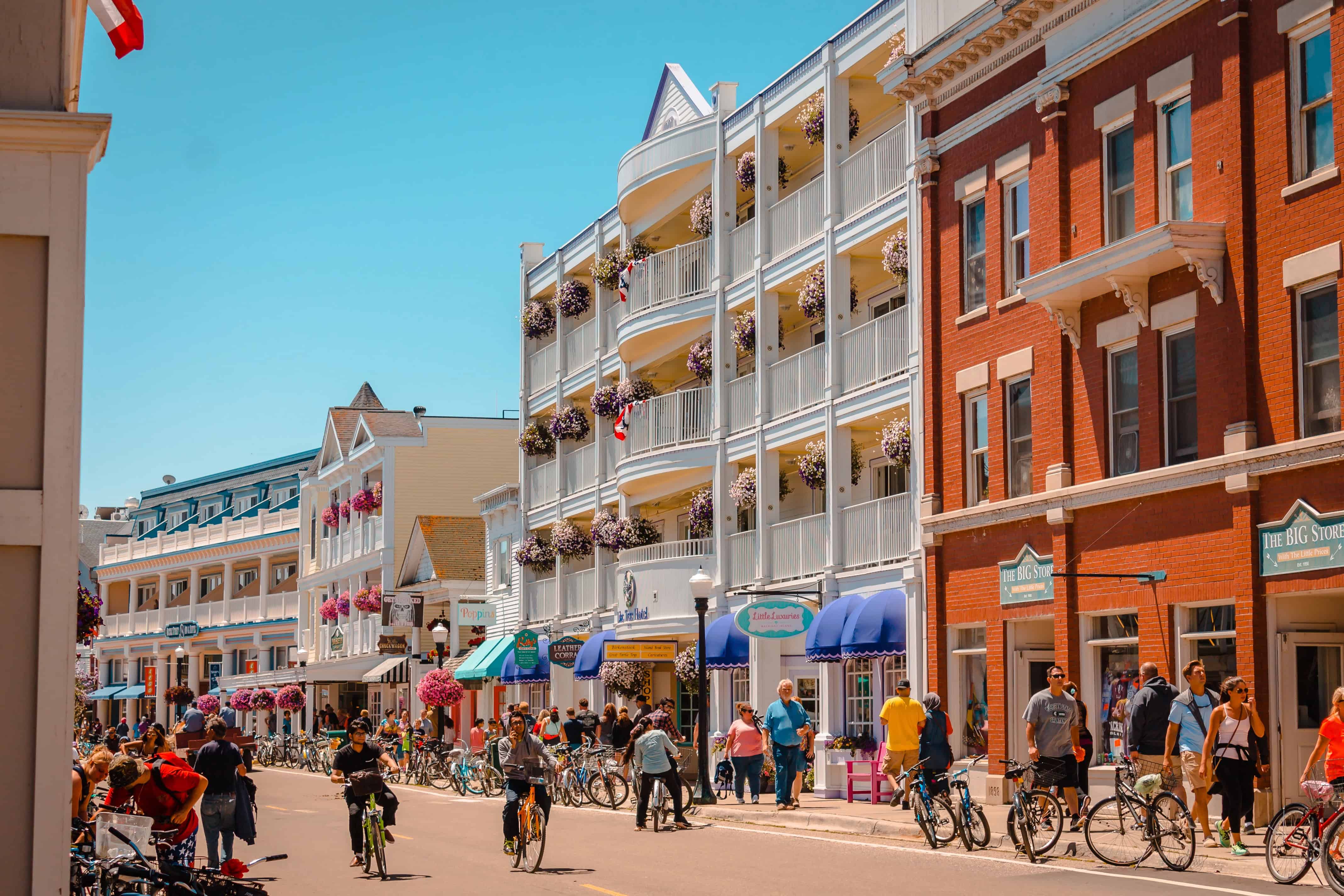 People walk and ride bikes along a lively street lined with colorful shops and flower-filled balconies, enjoying views that rival the best fall foliage in USA.