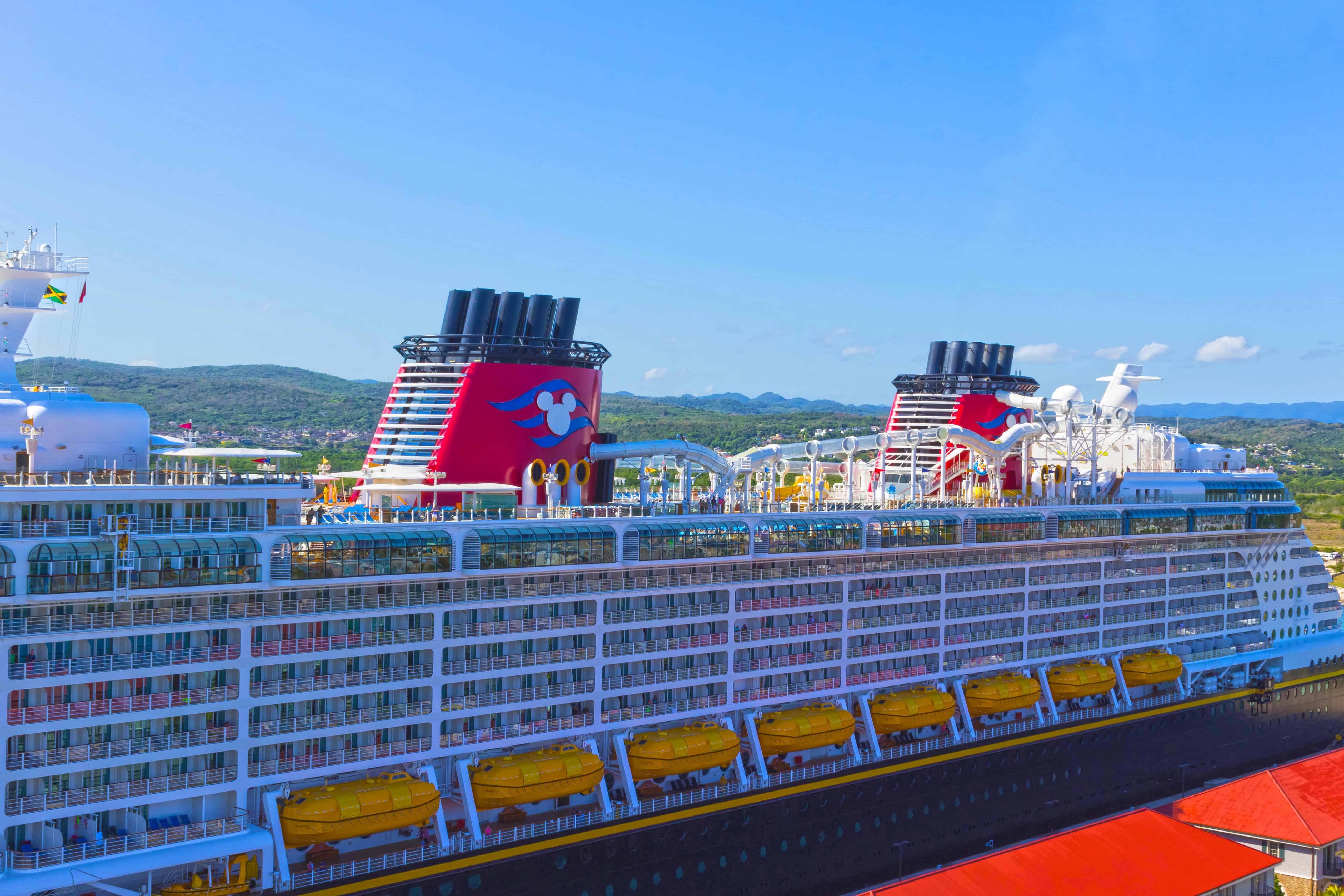 A large Disney cruise ship docked at a port, with hills and blue sky in the background—perfect for cruises for families seeking adventure or relaxation.