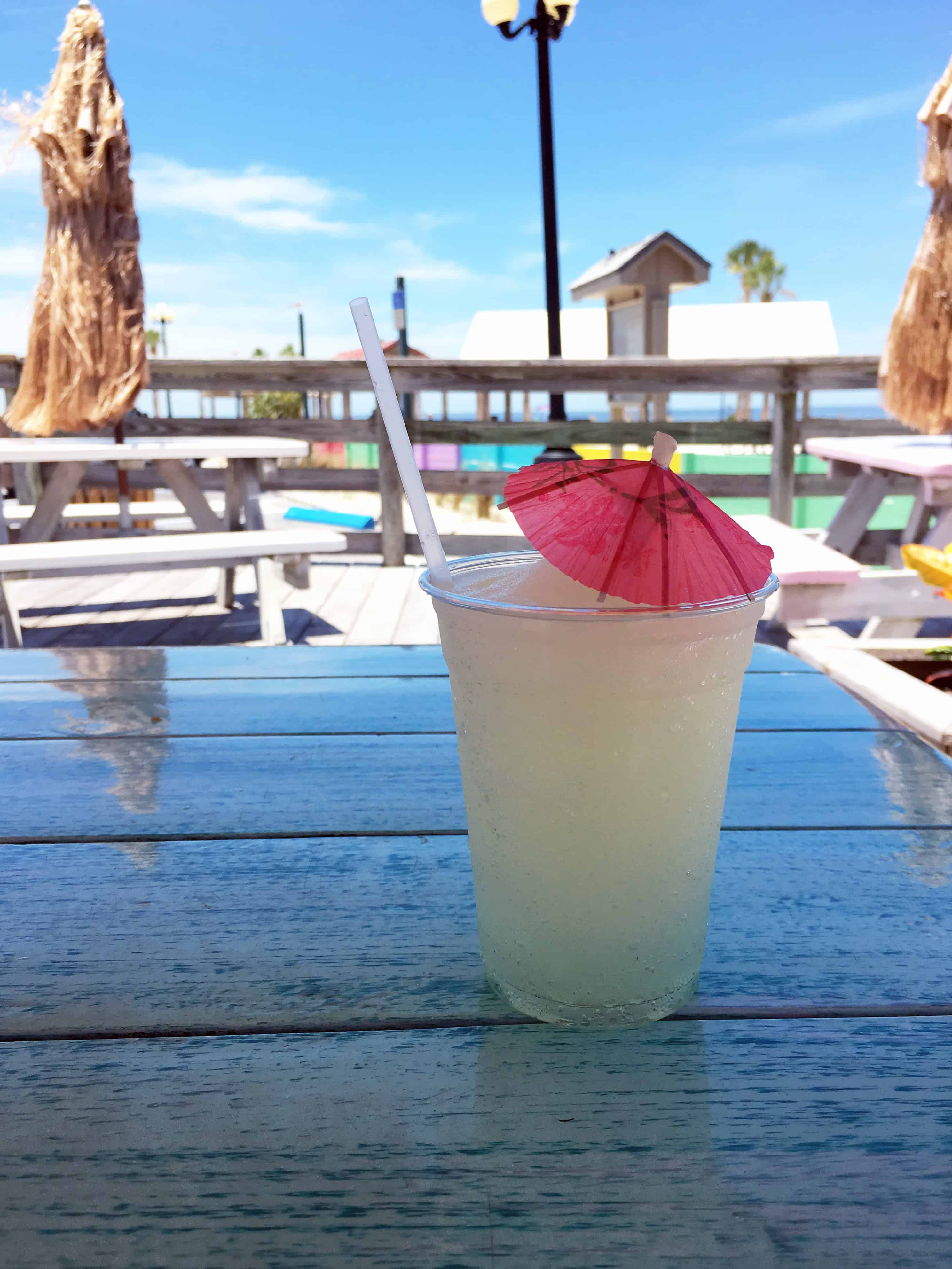 A lemonade with a pink umbrella sits on a picnic table at a sunny outdoor beachside cafe, perfect for relaxing after exciting Bahamas Cruise Activities for Families.