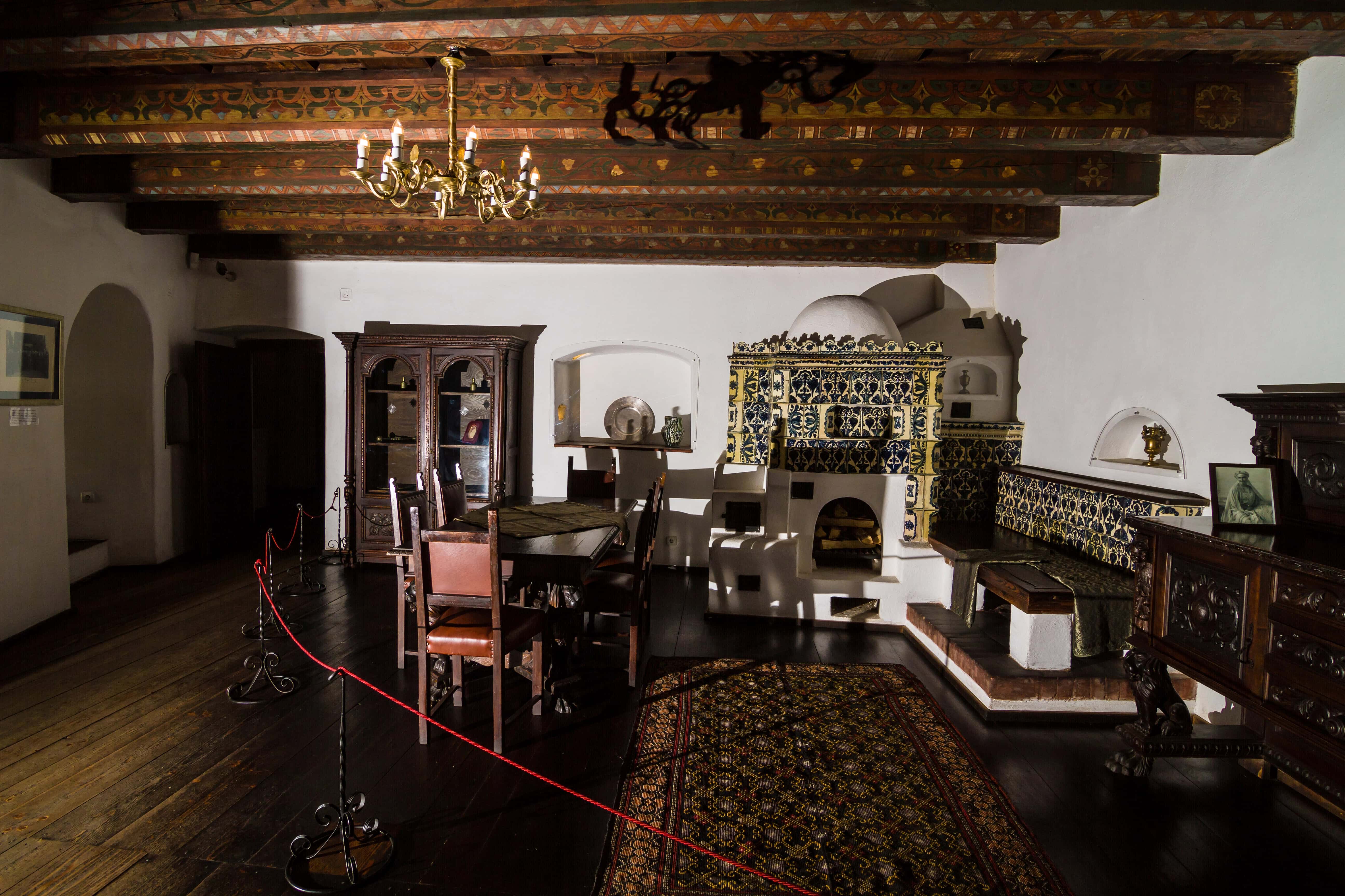 A historic room with wooden beams, antique furniture, a tiled stove, and a patterned rug—reminiscent of the mysterious charm found in haunted places in Europe.