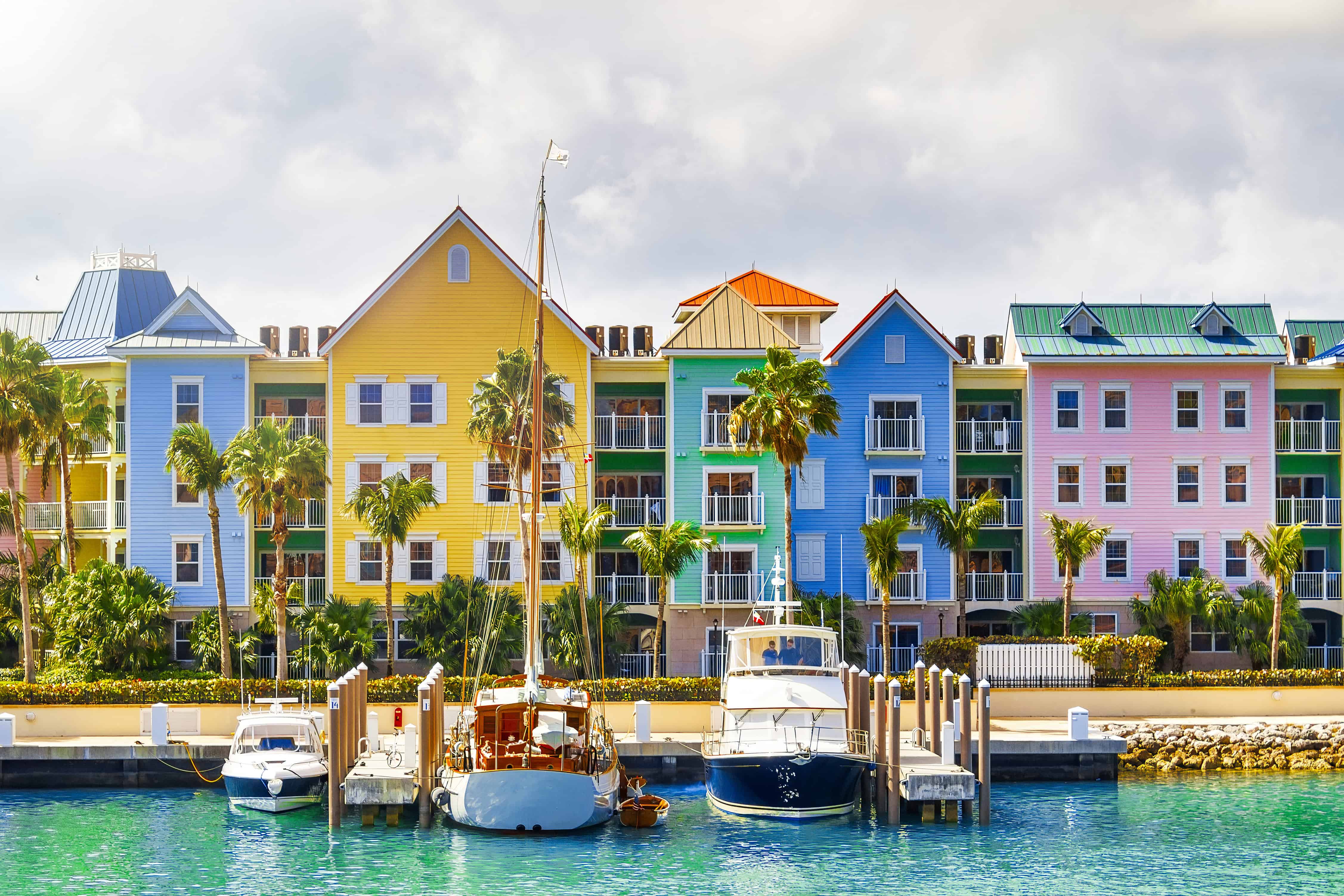 Colorful waterfront buildings and boats docked at a marina under a partly cloudy sky, offering a glimpse of the vibrant Bahamas cruise activities for families.
