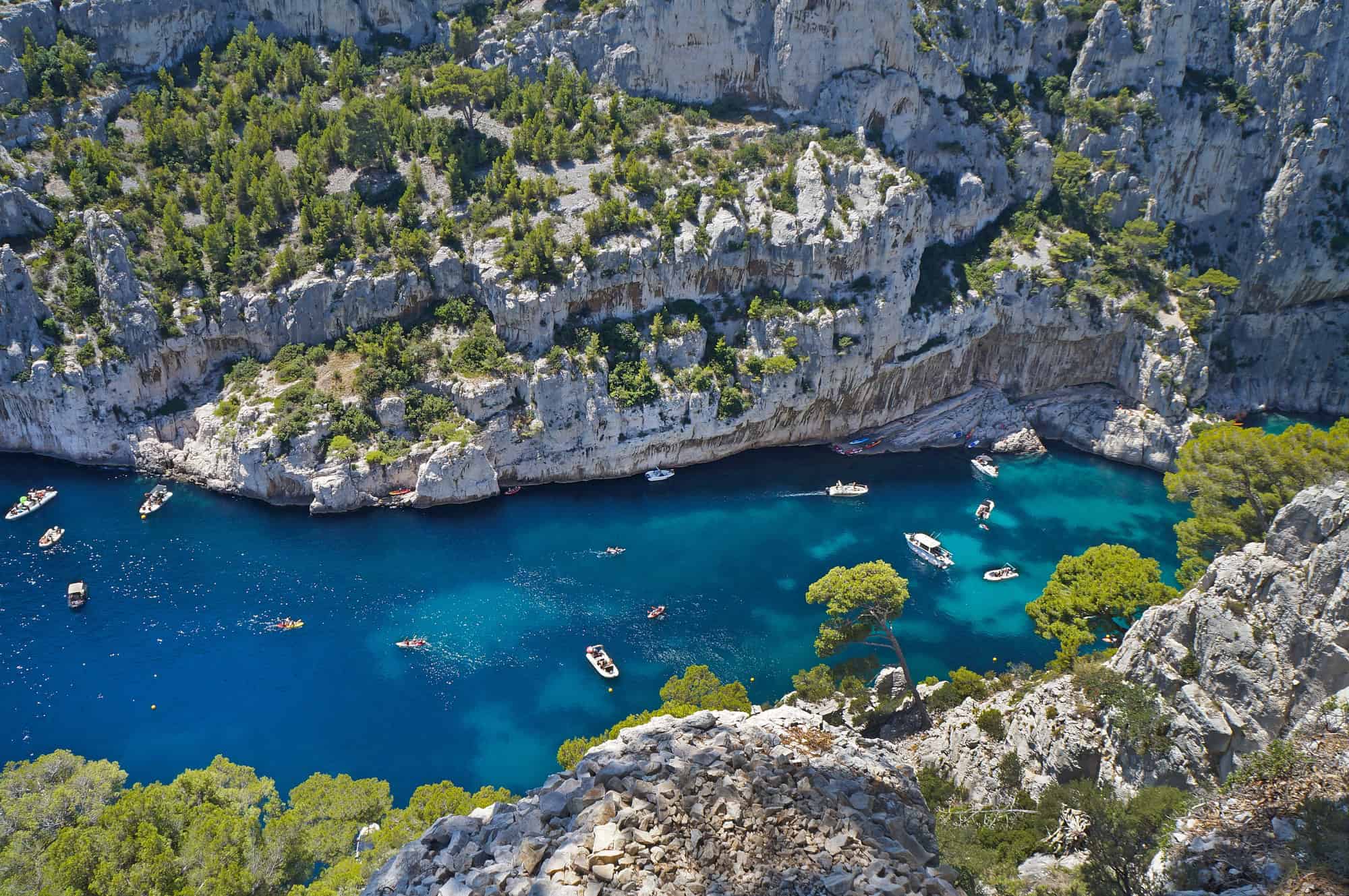 Boats float in a turquoise inlet near Marseille, France, surrounded by rocky cliffs and lush green trees—an idyllic stop on any itinerary.