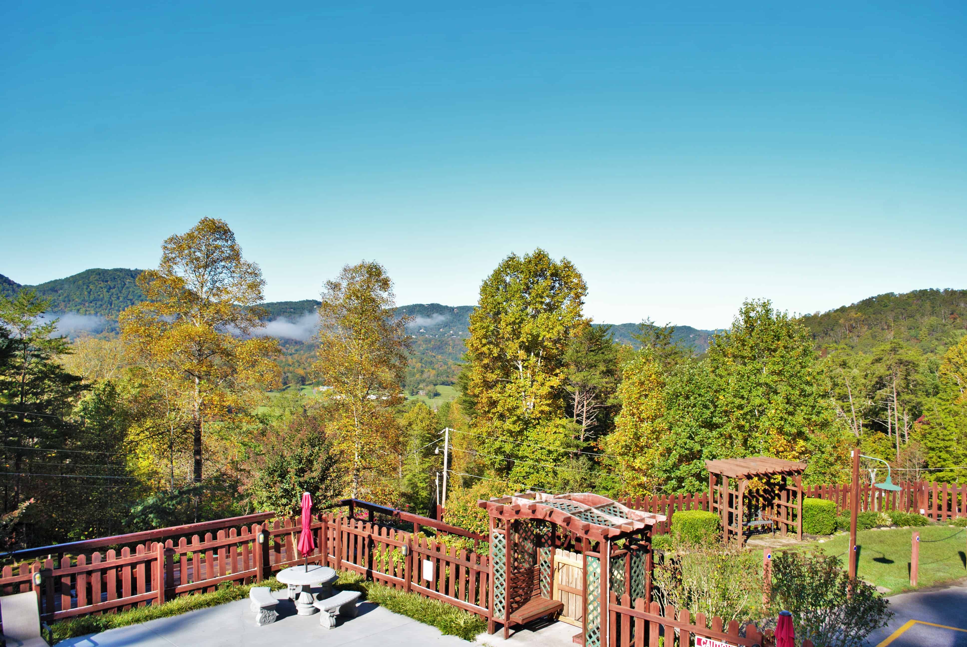 Mountain landscape with trees, a clear blue sky, and a fenced patio featuring seating and wooden pergolas—one of the best mountain getaways for relaxation and stunning views.