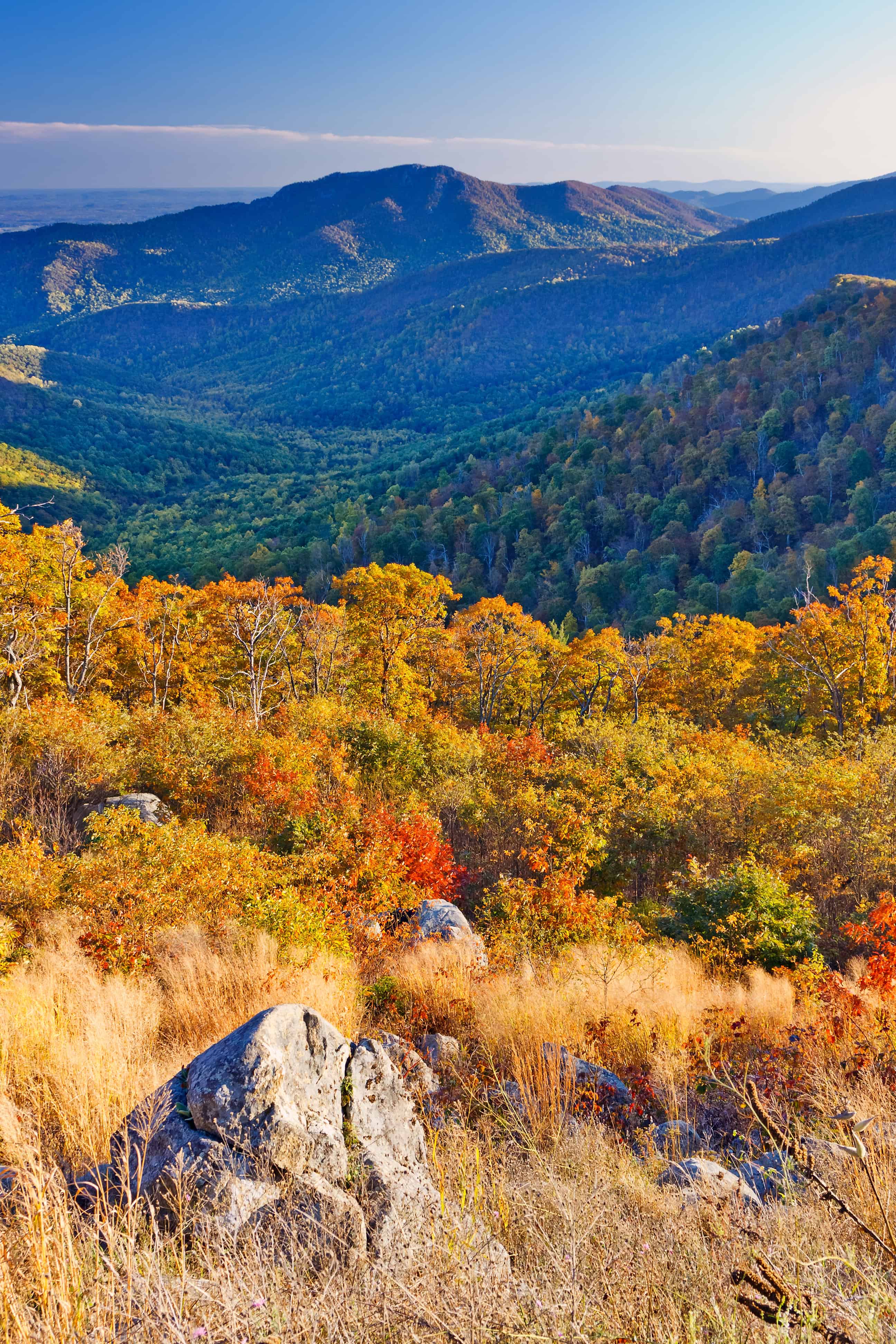 Scenic mountain landscape with autumn foliage, rolling hills, and rocks in the foreground under a clear sky—perfect for experiencing some of the best fall foliage in USA.