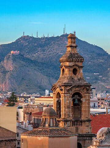 Rooftops and a historic church tower with a mountain in the background at sunset in Palermo, Sicily—a perfect scene to capture while exploring what to do in Palermo for a day.