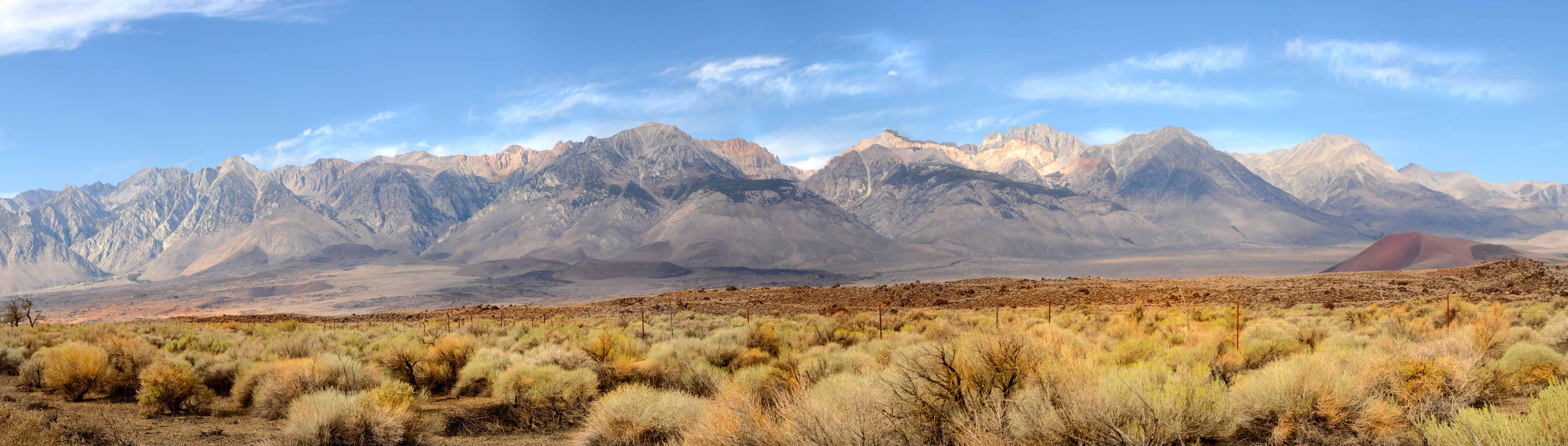 Panoramic view of a dry, grassy plain with rugged mountains under a blue sky with wispy clouds, reminiscent of regions known for the best fall foliage in USA.